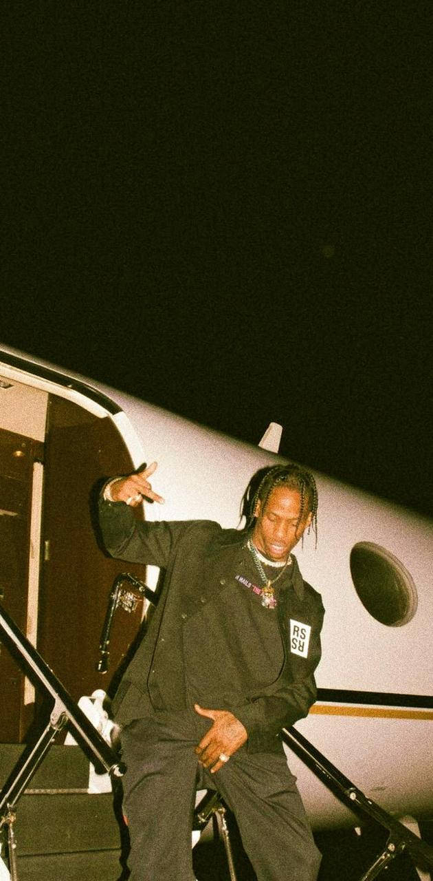 Travis Scott Aesthetic 桌布 壁紙 — 一名身穿黑色服裝的男子在夜間黑暗天空下的私人飛機樓梯上自信地擺姿勢。