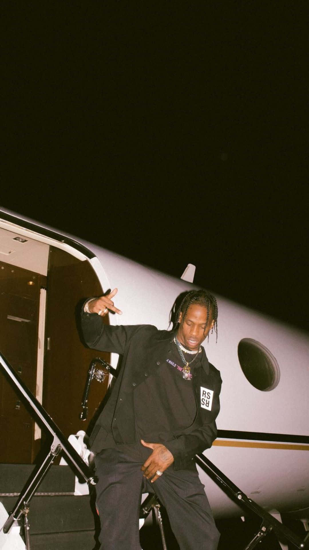Aesthetic Rapper 桌布 壁紙 — 一名身穿黑色服裝的男子在漆黑的夜空下，自信地站在私人飛機的樓梯上擺姿勢。