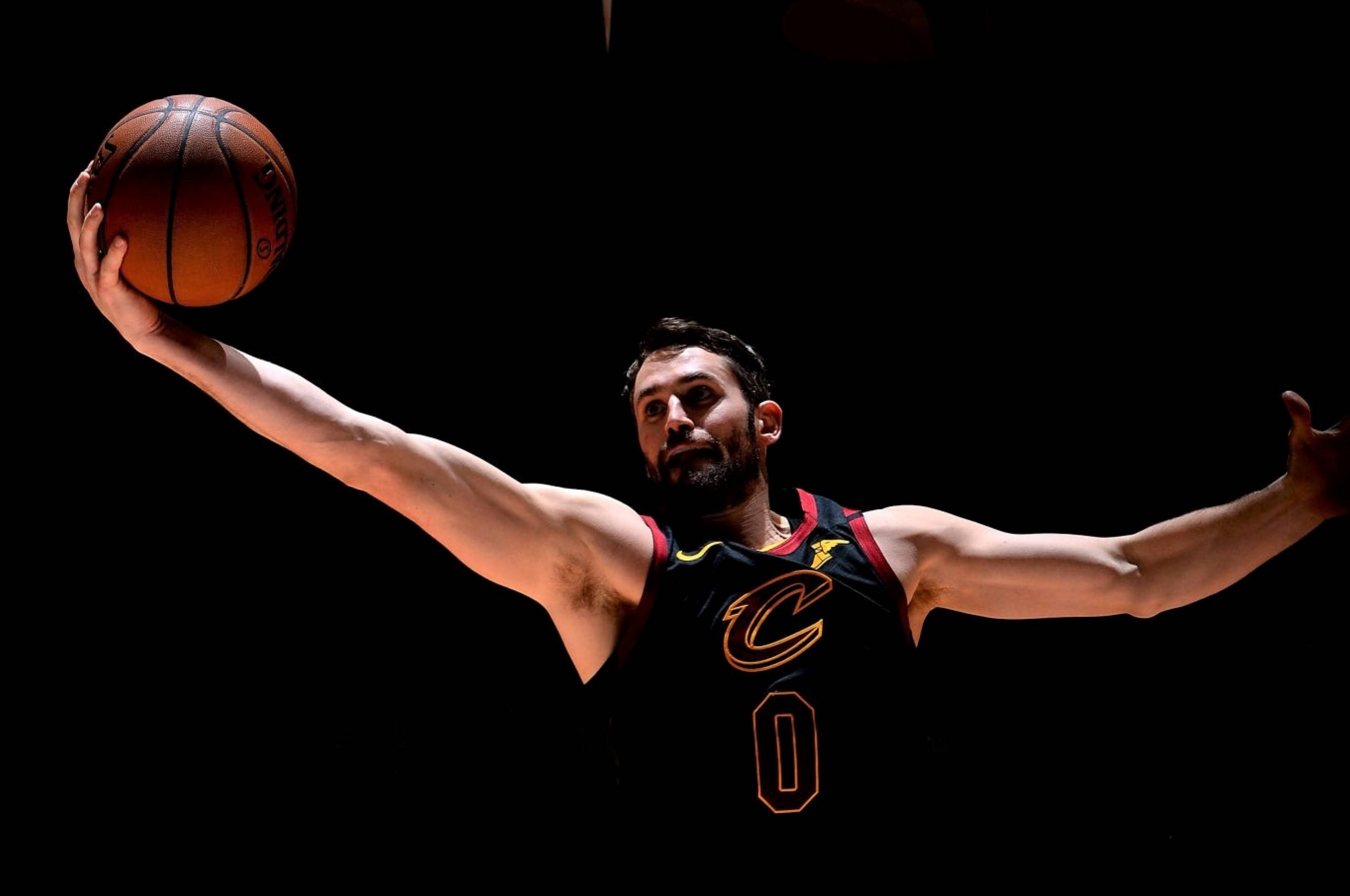 Kevin Love 桌布 壁紙 — 一名身穿黑色橙色飾邊球衣的籃球運動員，在純黑背景上高舉籃球。