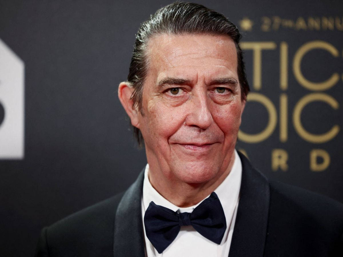 oscars 桌布 壁紙 — 一名身穿黑色燕尾服和領結的男子在正式活動中微笑的特寫肖像，背景為深色並帶有金色文字。