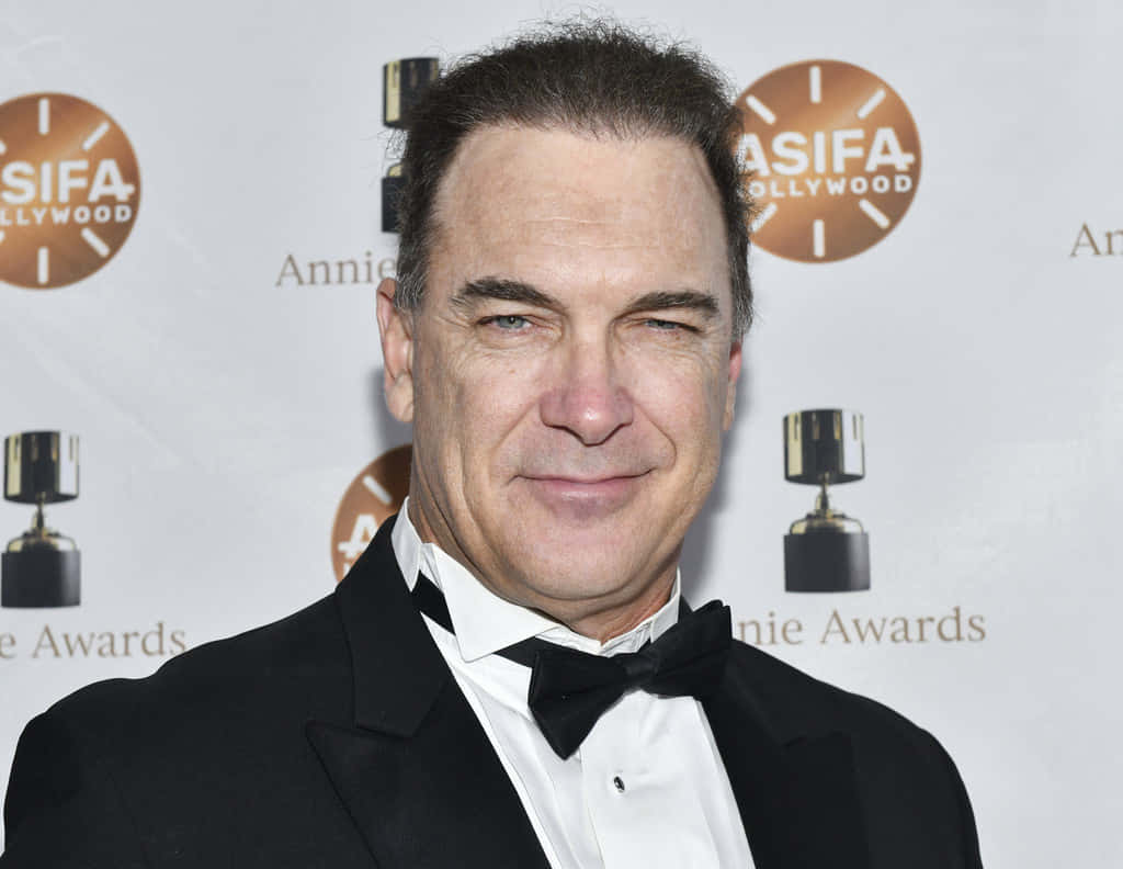 Patrick Warburton 桌布 壁紙 — 一名身穿黑色燕尾服和領結的男子在白色背景前微笑，背景上有ASIFA Hollywood和Annie Awards標誌。