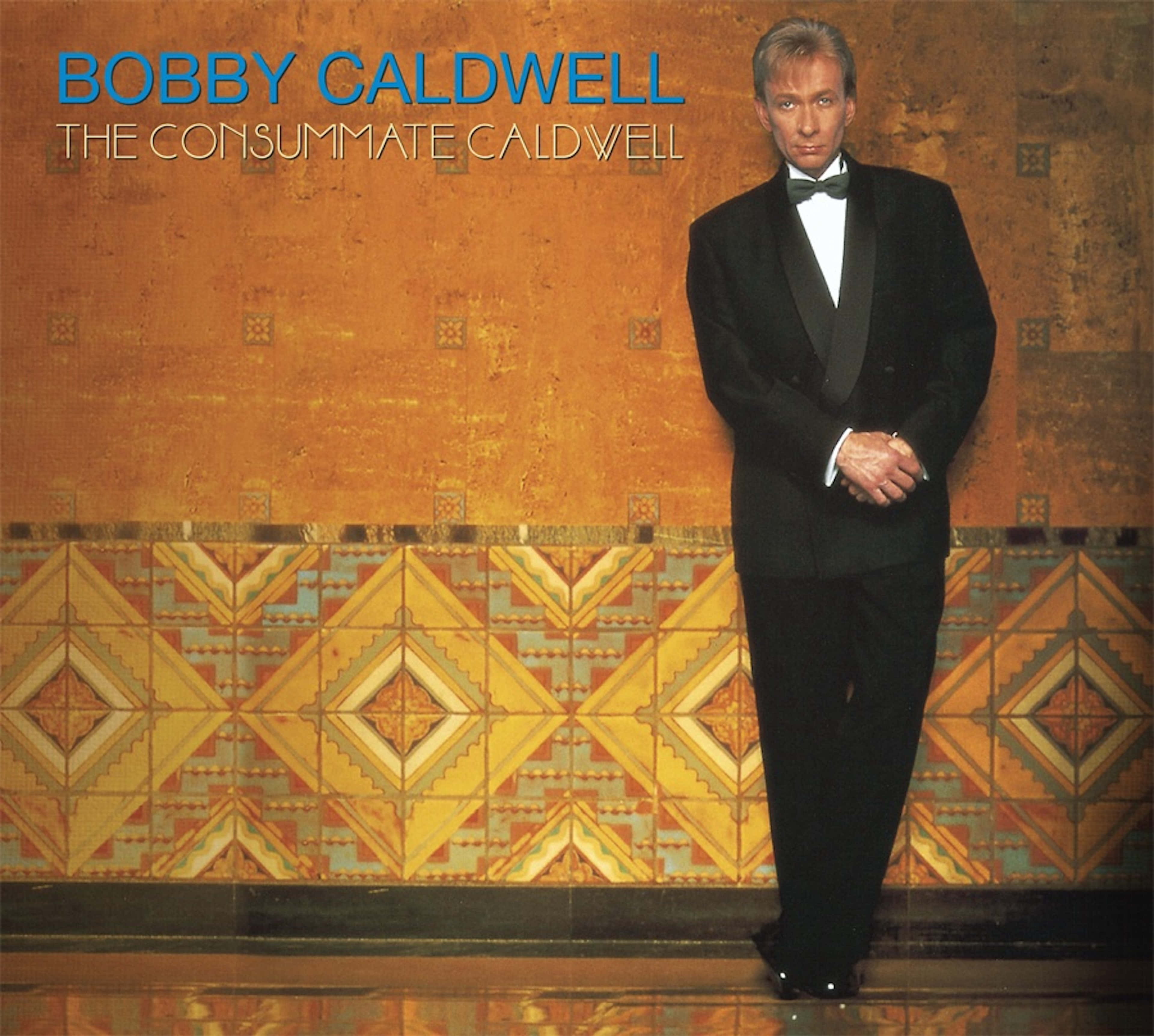 Bobby Caldwell 桌布 壁紙 — 一名身穿黑色燕尾服的男士，優雅地站在暖色調的牆前，牆上有幾何瓷磚圖案。
