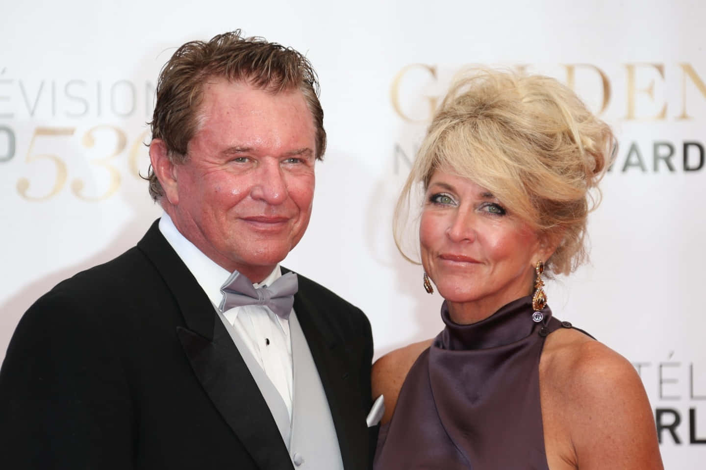 Tom Berenger 桌布 壁紙 — 一名身穿黑色燕尾服的男士和一名身穿紫色連衣裙的女士在金球獎紅地毯上合影。