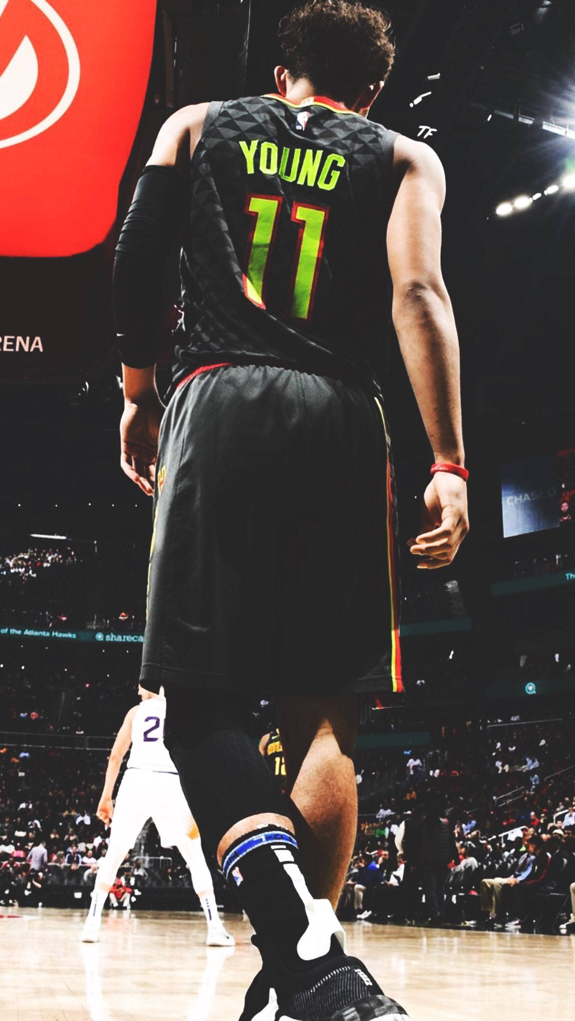 Trae Young 桌布 壁紙 — 一名身穿黑色球衣、上面有螢光綠色「YOUNG 11」字樣的籃球運動員，在燈光明亮的球場上背對鏡頭走開。