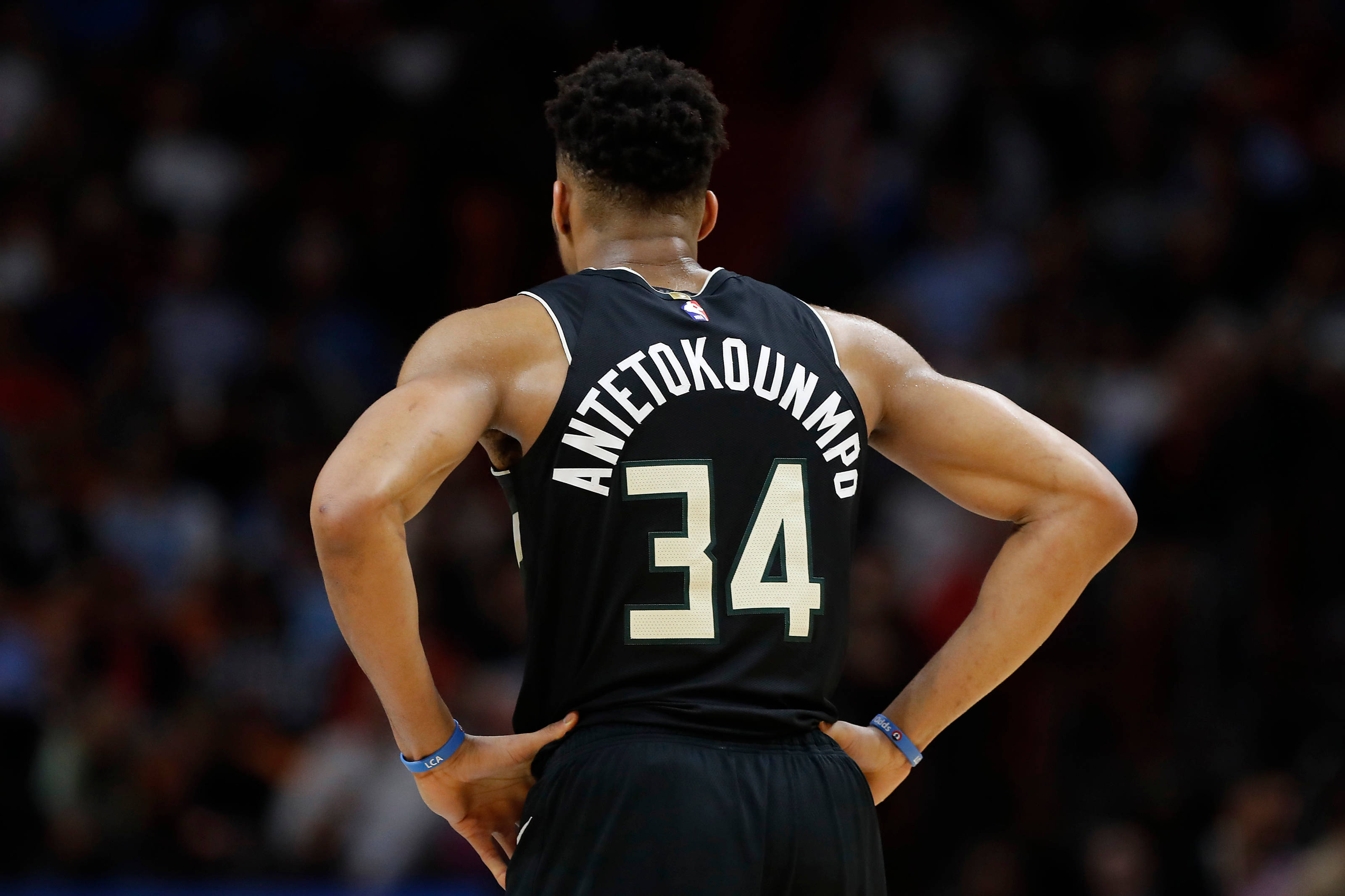 Giannis 桌布 壁紙 — 一名身穿黑色球衣、印有名字Antetokounmpo和號碼34的籃球運動員，雙手叉腰，背對鏡頭站立。