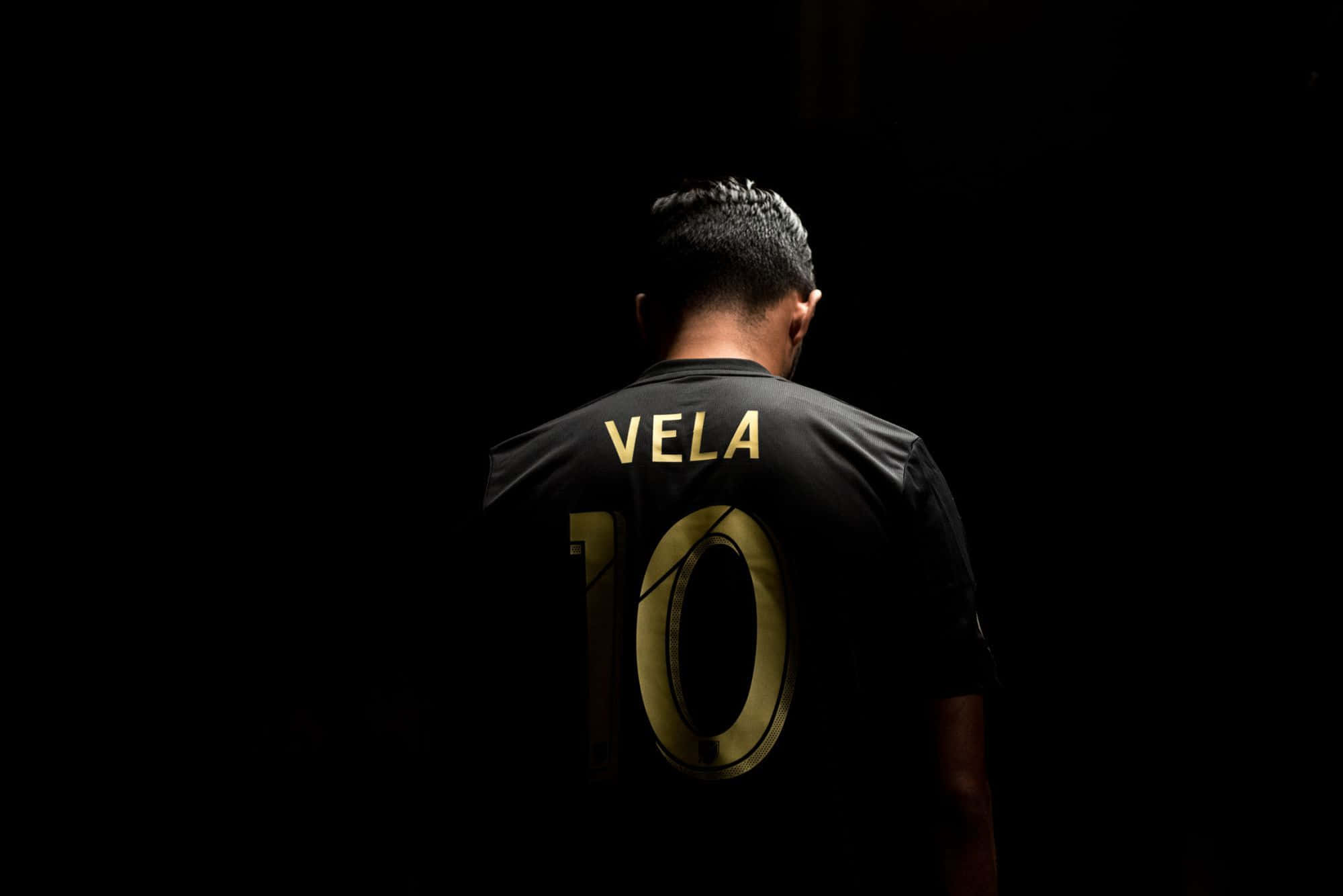 Handsome Boy 桌布 壁紙 — 一名身穿黑色球衣、印有金色「VELA 10」的足球運動員站在黑暗中，背光凸顯名字和號碼。