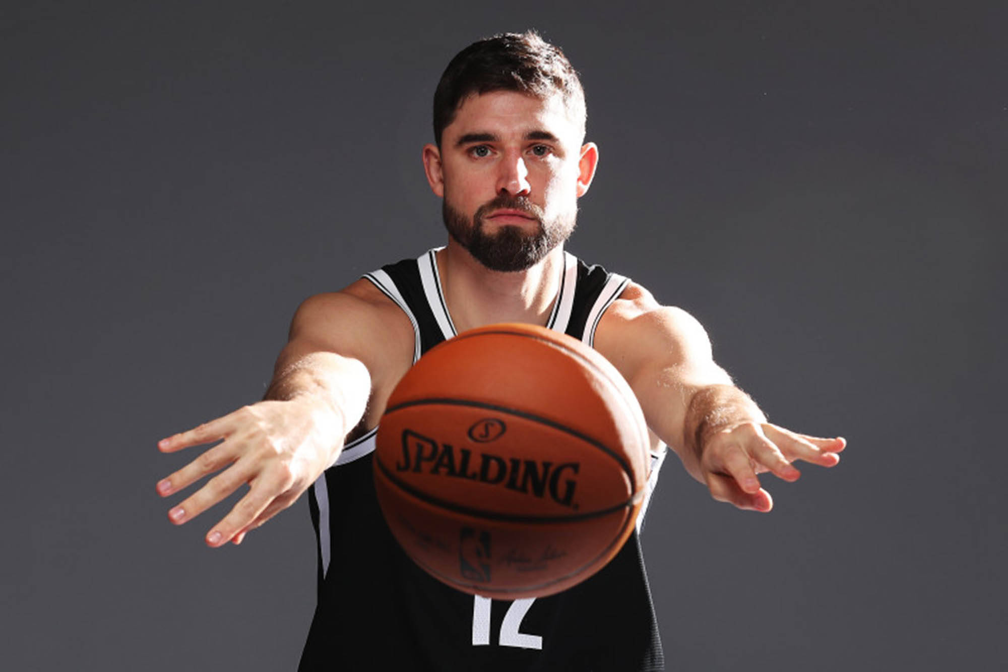 joe harris 桌布 壁紙 — 一名身穿黑色球衣、專注的籃球運動員，在深色攝影棚背景下向Spalding球伸出雙臂。