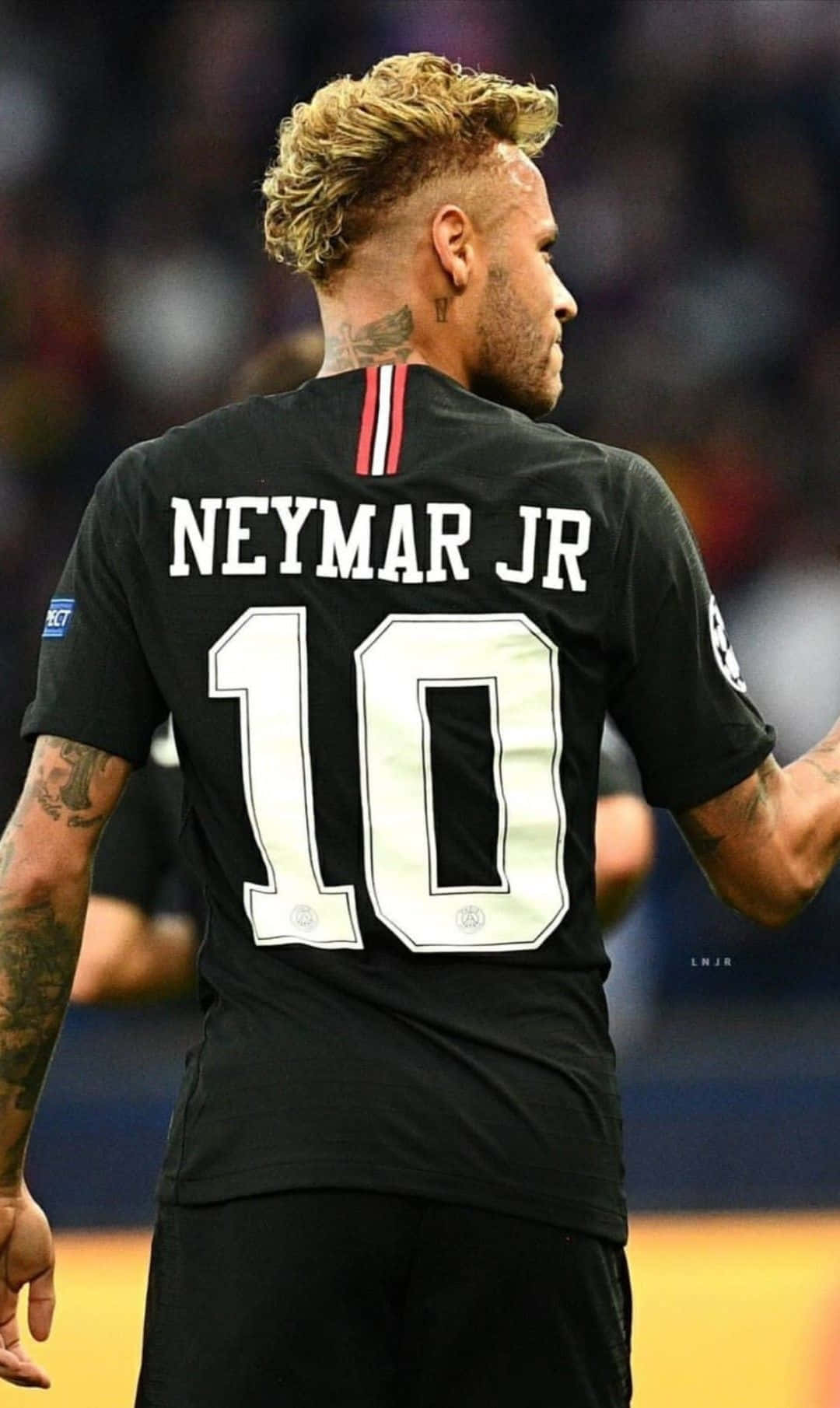 内马尔 桌布 壁紙 — 一名身穿黑色球衣、背後印有「NEYMAR JR」和10號的足球員站在球場上，背景是模糊的體育場燈光。