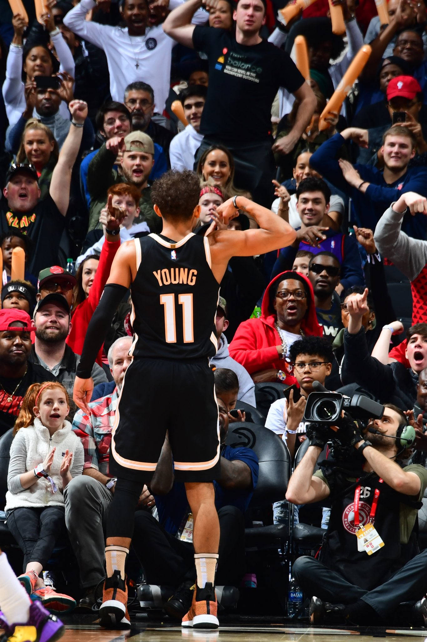 Trae Young 桌布 壁紙 — 一名身穿黑色球衣、背號11、名字為Young的籃球運動員在比賽中向興奮的人群展示肌肉。