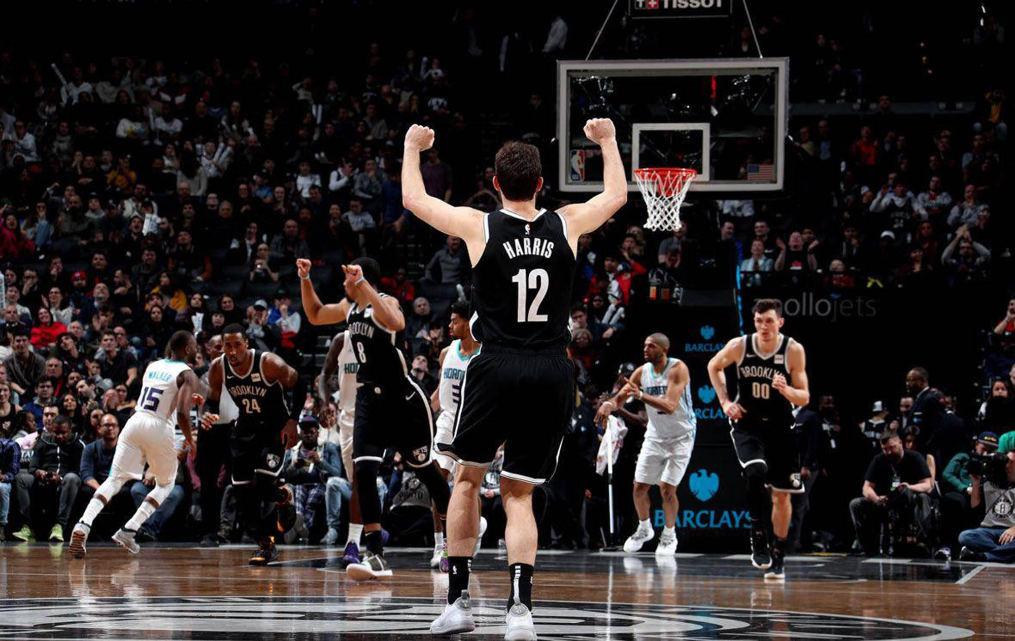 joe harris 桌布 壁紙 — 一名身穿黑色球衣、背號12的籃球運動員在明亮的場館燈光下高舉拳頭慶祝勝利，隊友和對手在球場上作出反應。
