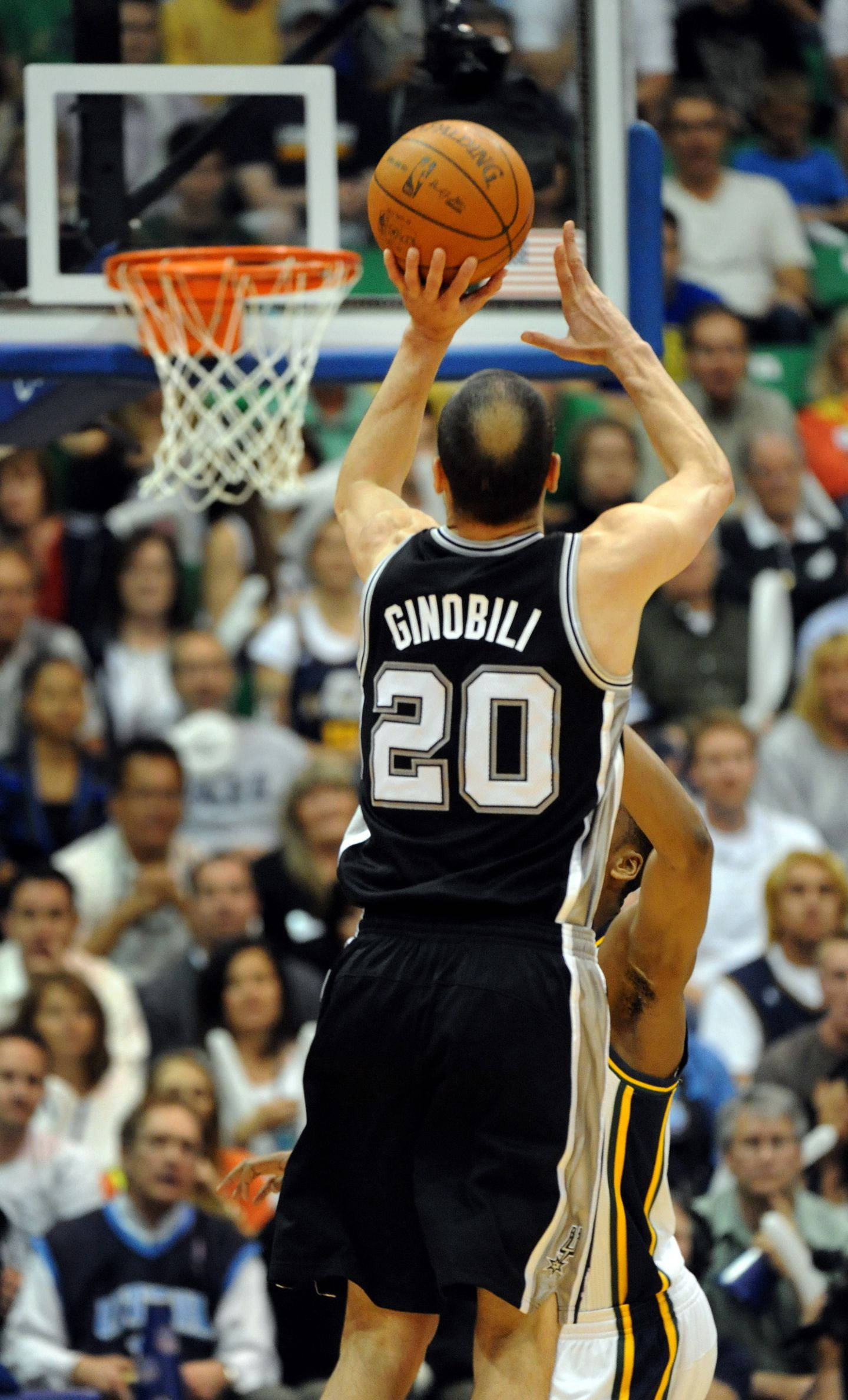 Manu 桌布 壁紙 — 一名身穿黑色球衣、背號20的籃球運動員在明亮的場館燈光下跳起投籃，而一名防守球員躍起封阻。
