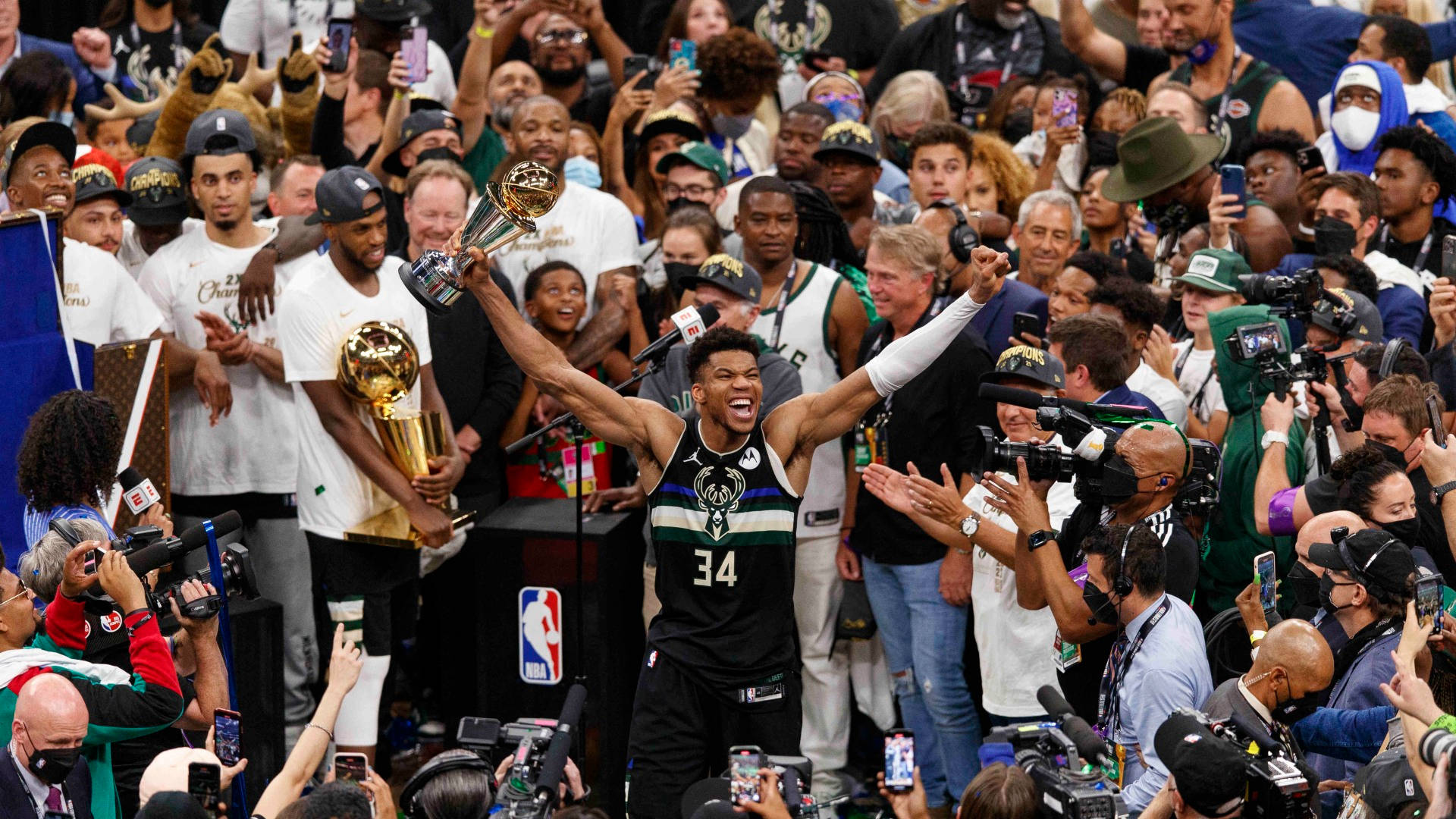 finals 桌布 壁紙 — 一名身穿黑色球衣、背號34的籃球運動員在歡呼的球迷和媒體包圍下，勝利地將金色獎盃高舉過頭頂。