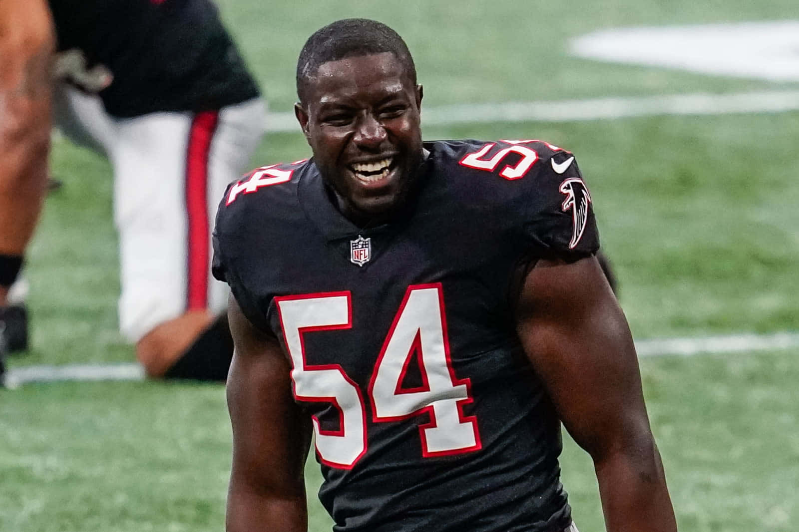 Atlanta Falcons 桌布 壁紙 — 一名身穿黑色球衣、號碼54的美式足球員在球場燈光下的綠色草地上開懷大笑。