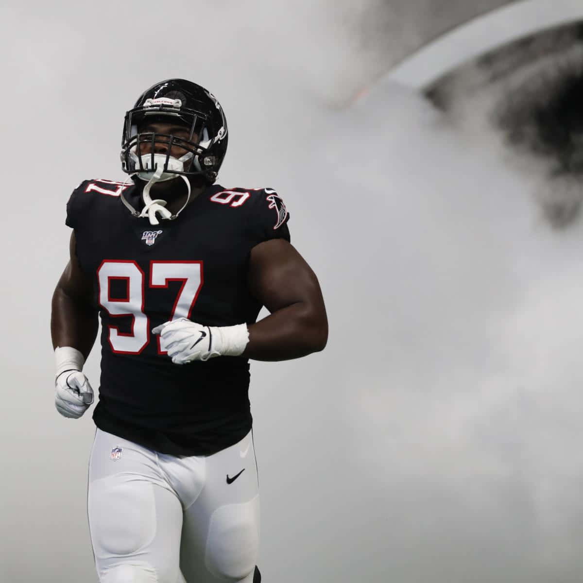 Atlanta Falcons 桌布 壁紙 — 一名身穿黑色球衣、號碼97的美式足球員在球場的煙霧中奔跑。