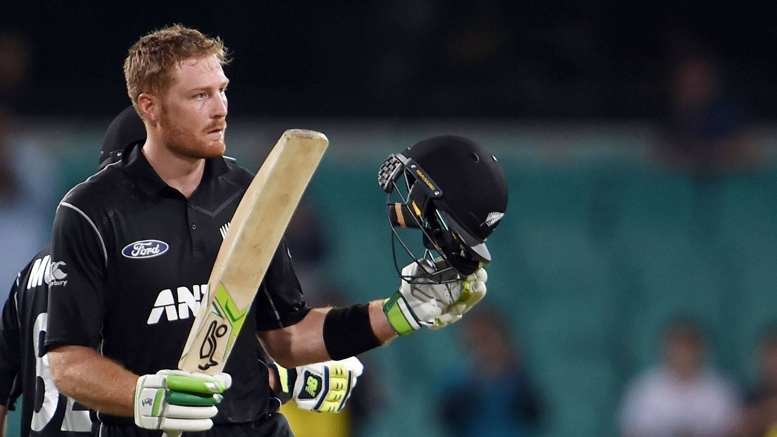 martin guptill 桌布 壁紙 — 一名身穿黑色球衣的板球運動員在球場燈光下，賽後手持球棒和頭盔。