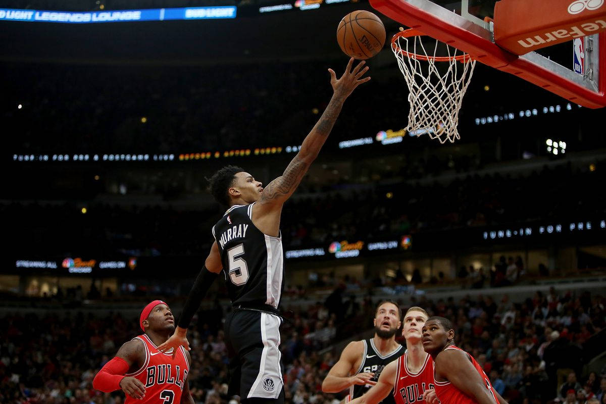 Dejounte Murray 桌布 壁紙 — 一名身穿黑色球衣的籃球運動員在場館燈光下跳起灌籃，防守球員專注地觀看。