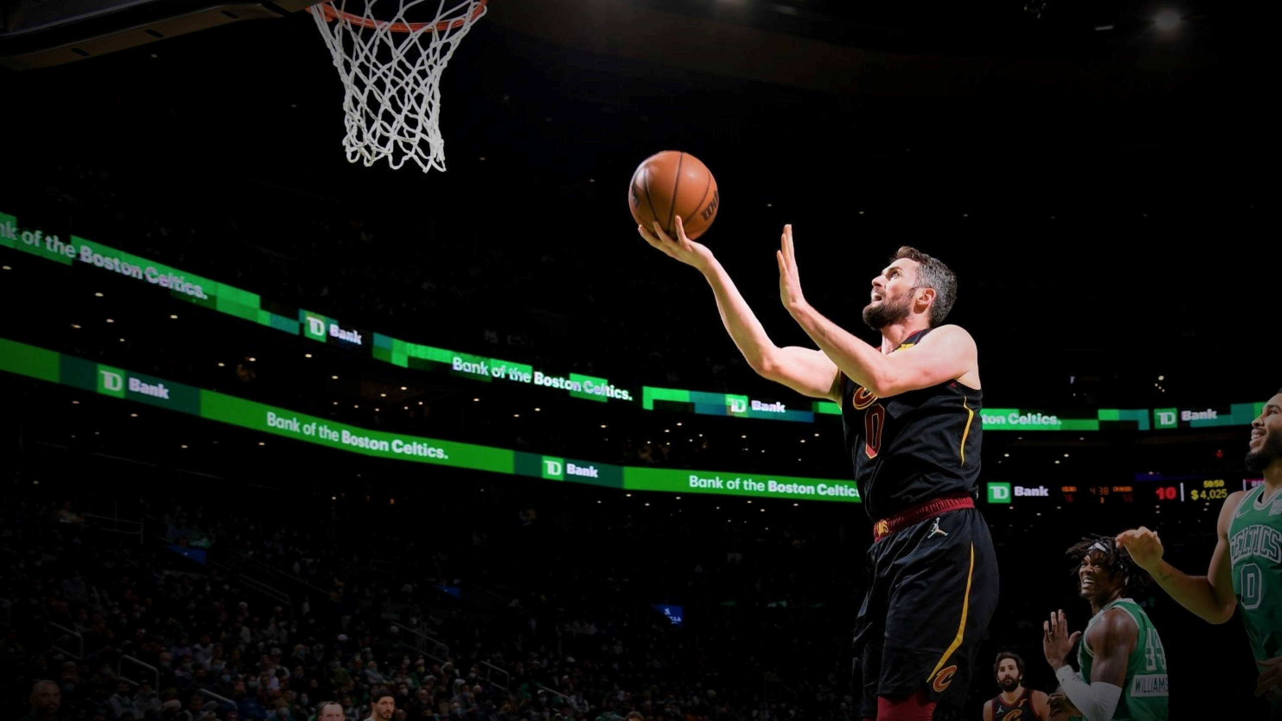 Kevin Love 桌布 壁紙 — 一名身穿黑色球衣的籃球運動員在明亮的場館燈光下跳起投籃，觀眾在旁觀看。