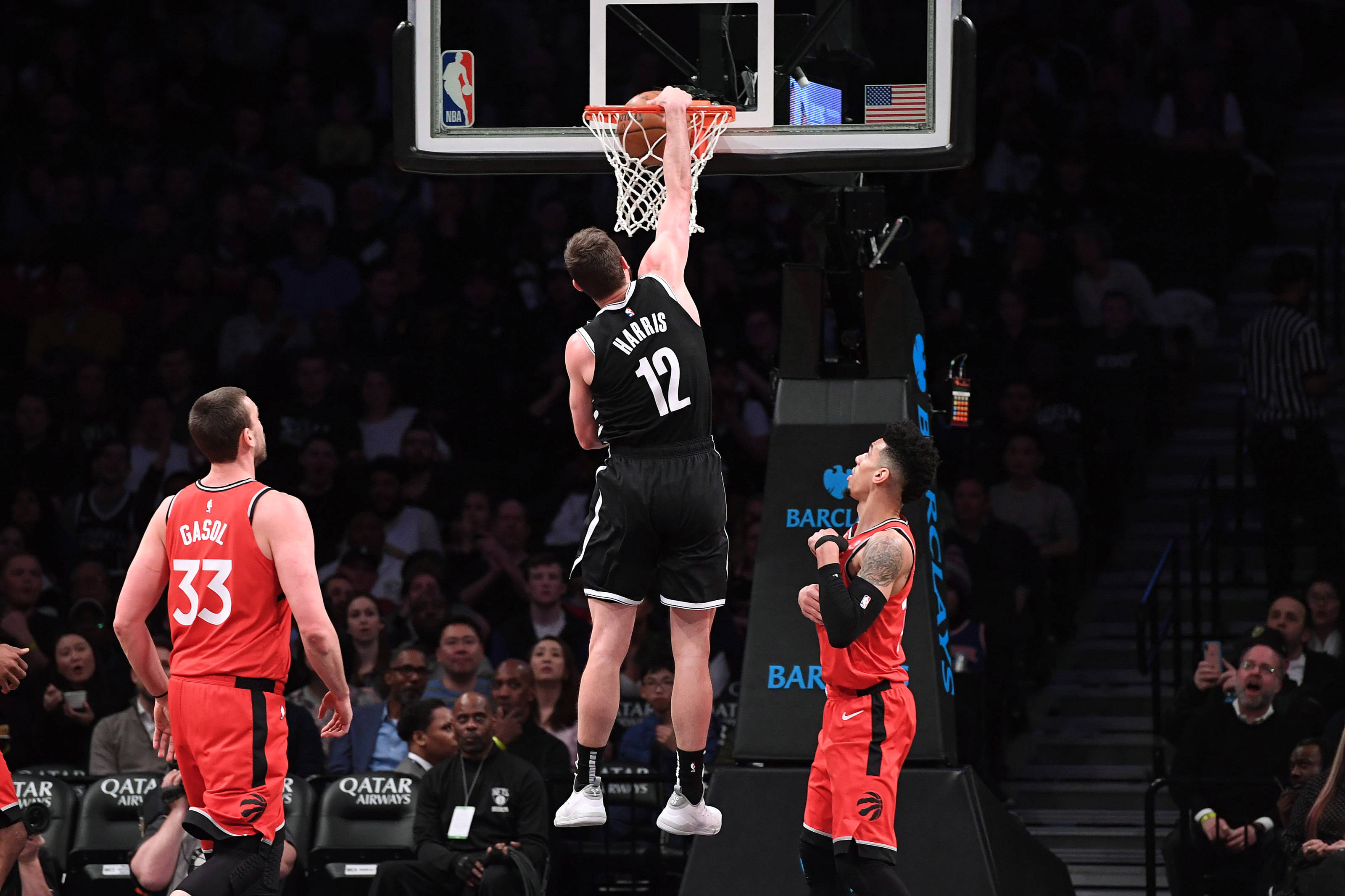 joe harris 桌布 壁紙 — 一名身穿黑色球衣的籃球運動員灌籃，兩名身穿紅色球衣的對手在擠滿人的場館中觀看。