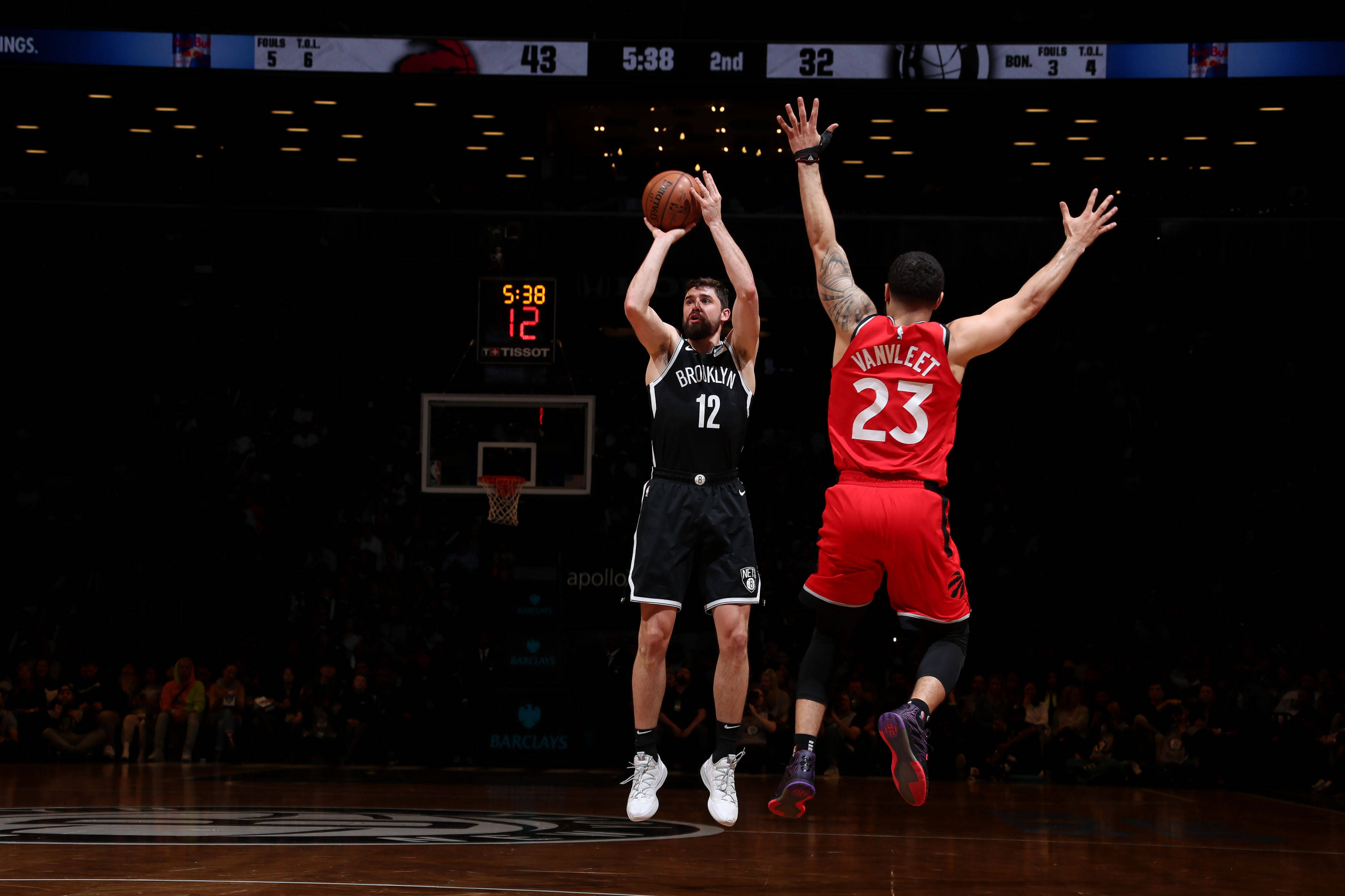 joe harris 桌布 壁紙 — 一名身穿黑色球衣的籃球運動員跳起投籃，而一名紅色球衣的防守者在場館燈光下跳起封阻。