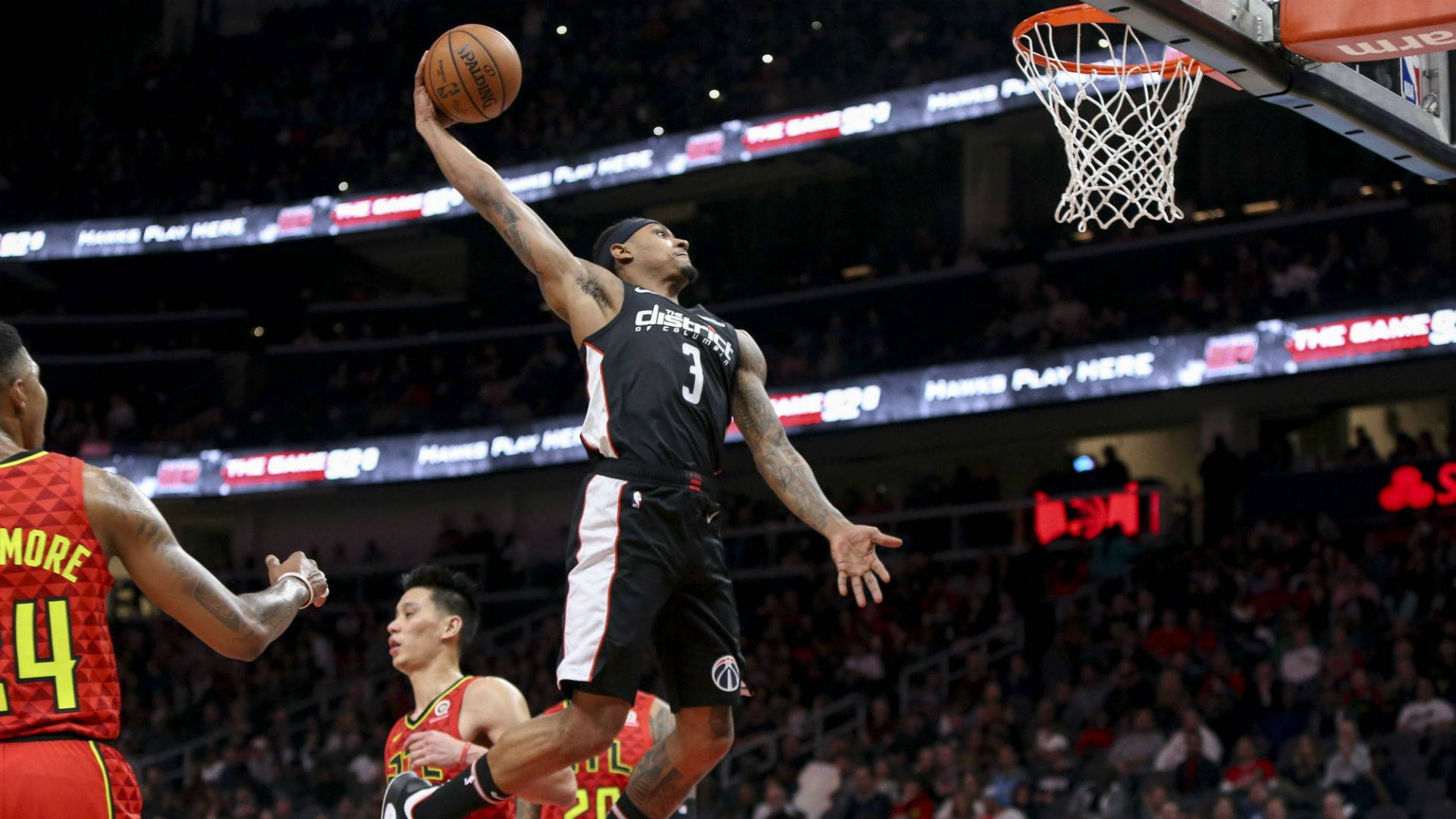 Bradley Beal 桌布 壁紙 — 一名身穿黑色球衣的籃球運動員高高躍起灌籃，下方防守球員在座無虛席的場館內觀望。