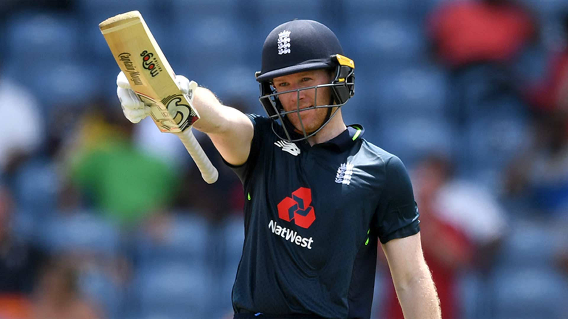 eoin morgan 桌布 壁紙 — 一名身穿黑色球衣的英格蘭板球選手在陽光明媚的比賽中，將球棒勝利地舉向天空。