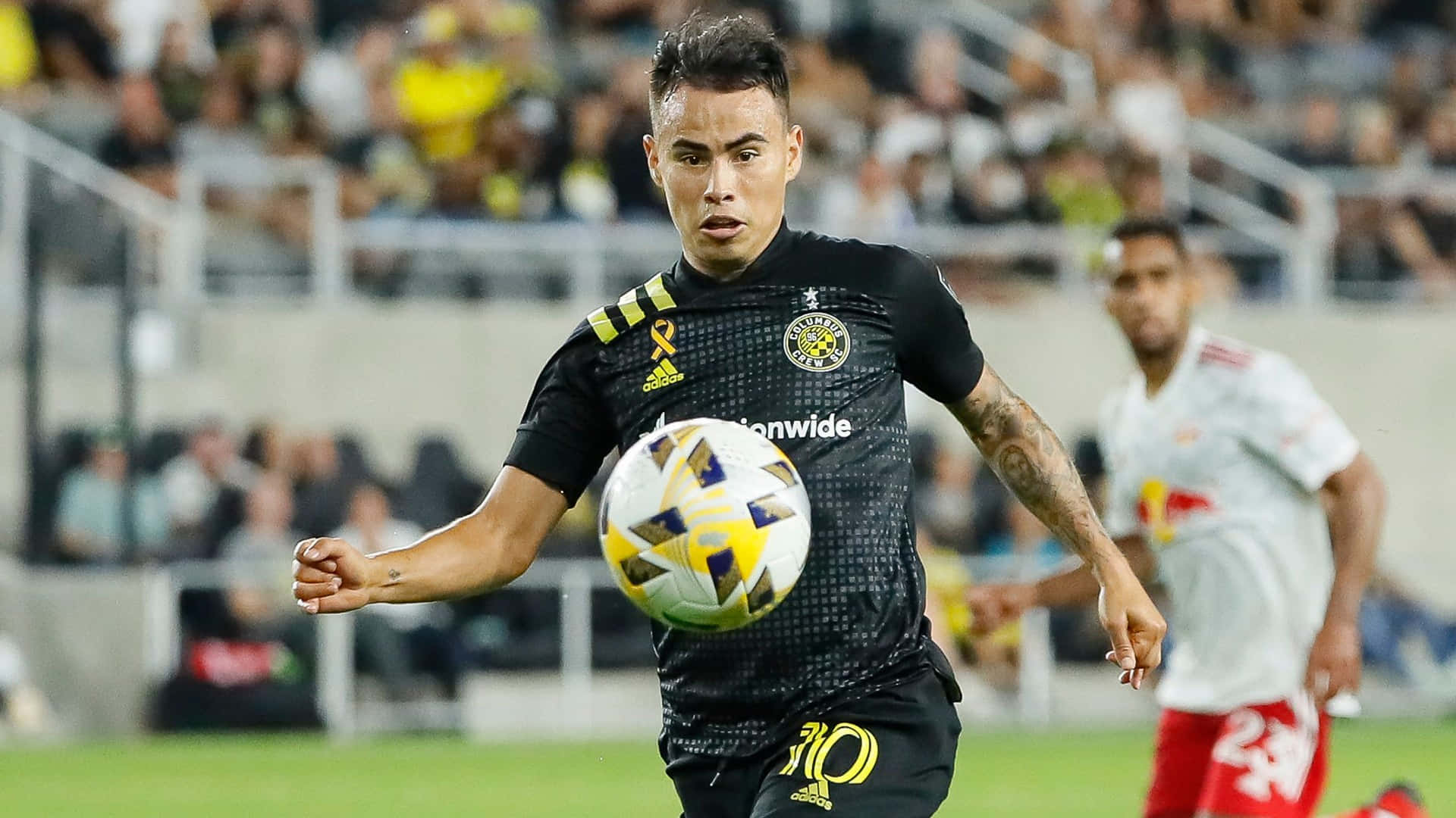 Soccer Ball 桌布 壁紙 — 一名身穿黑色球衣的足球運動員在球場燈光下的綠色場地上控制一個黃白相間的球。