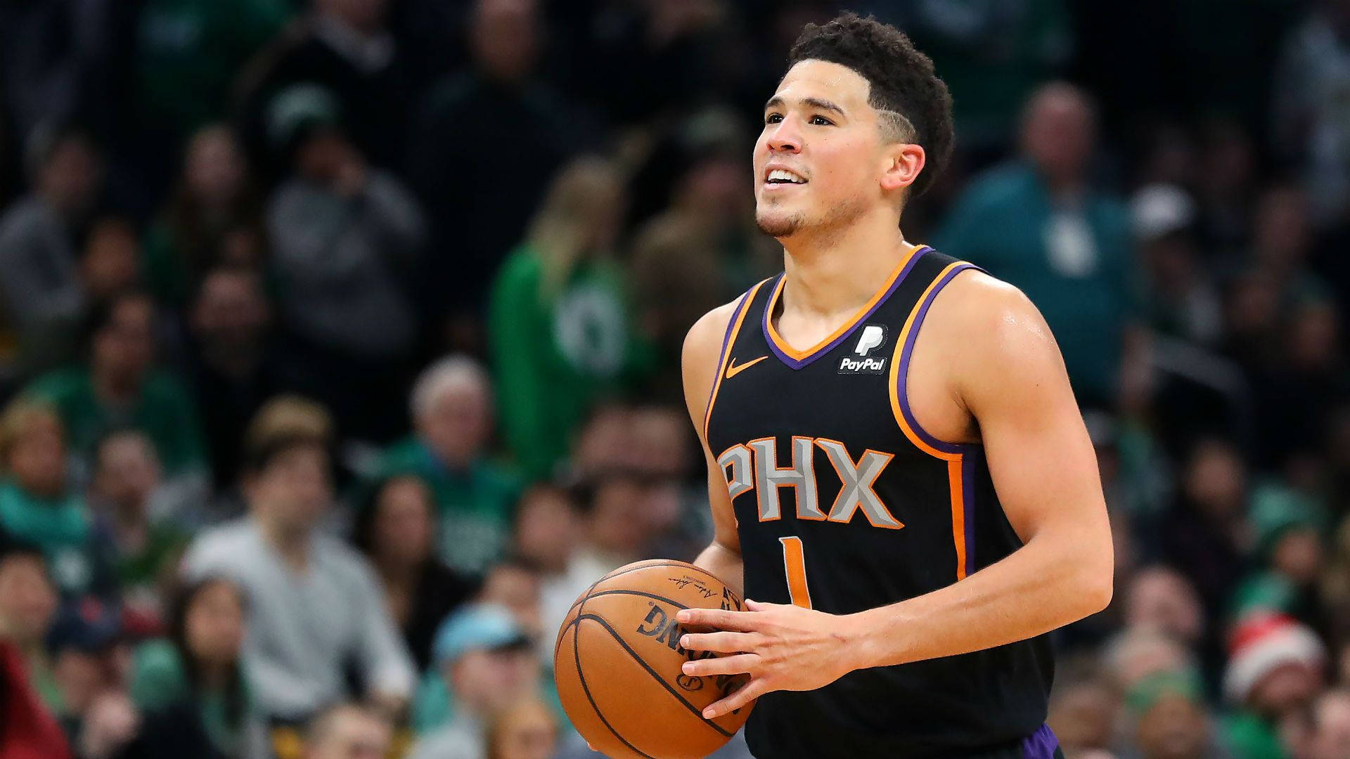 Devin Booker 桌布 壁紙 — 一名身穿黑色球衣的鳳凰城太陽隊籃球運動員在比賽中專注地持球，背景是模糊的人群。