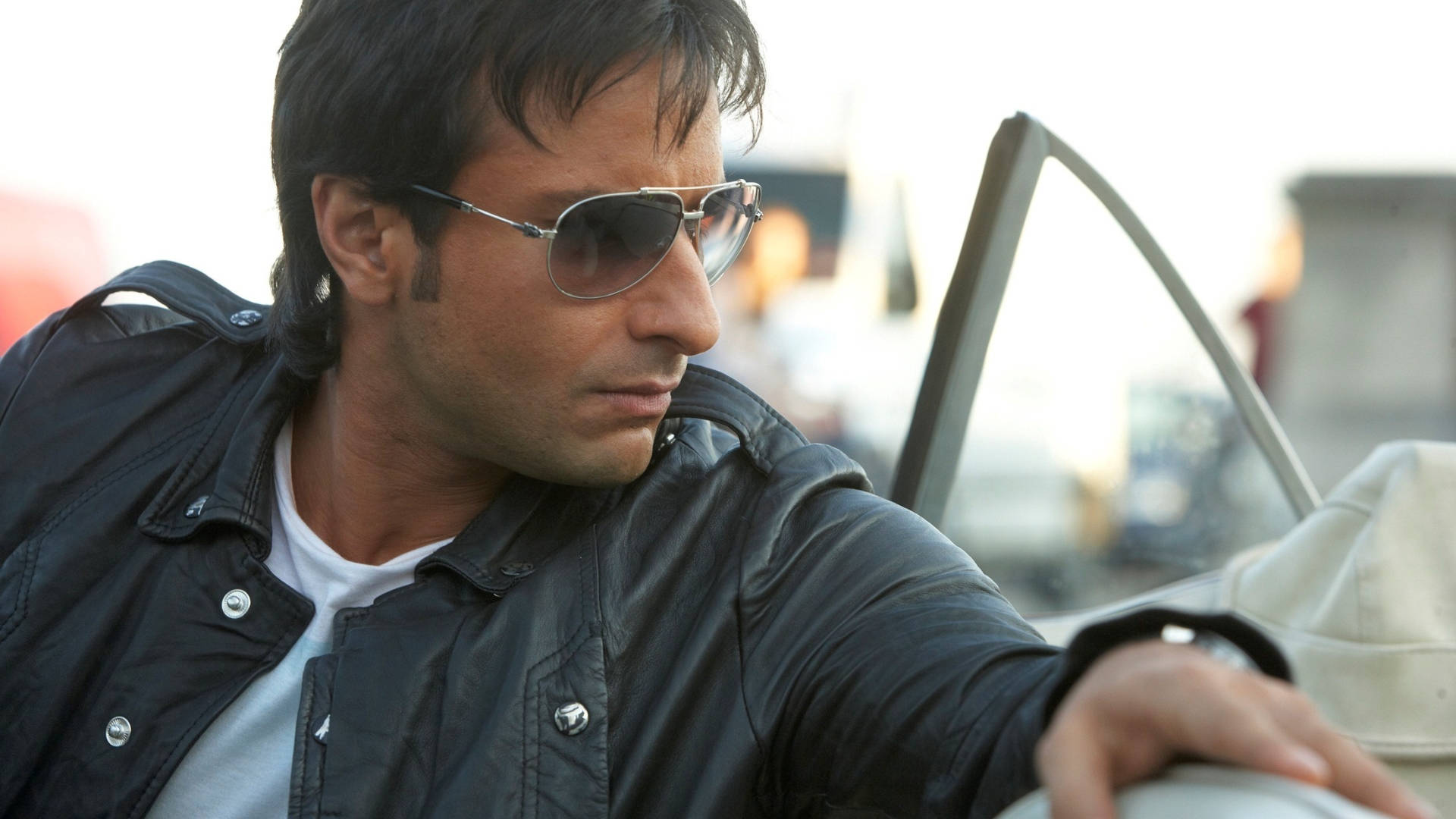 Saif Ali Khan 桌布 壁紙 — 一名身穿黑色皮夾克及戴著飛行員太陽眼鏡的男子，表情嚴肅地從車窗探出身子。