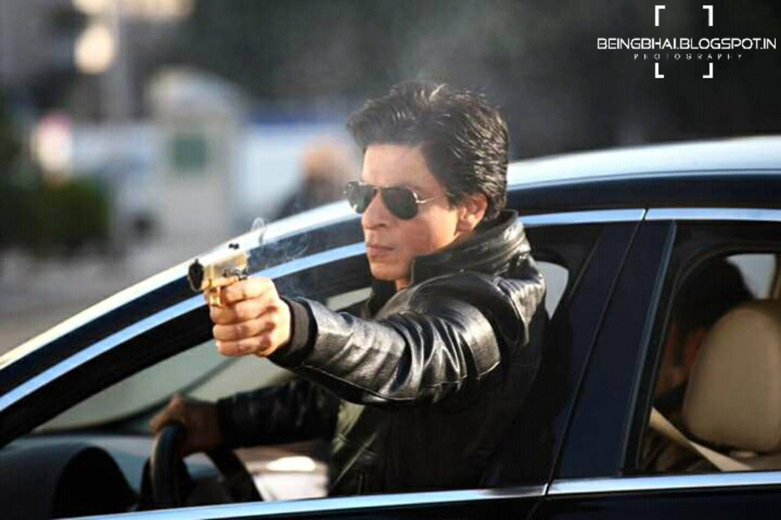 Shahrukh 桌布 壁紙 — 一名身穿黑色皮夾克和太陽眼鏡的男子在白天從車窗開槍，手槍冒煙。