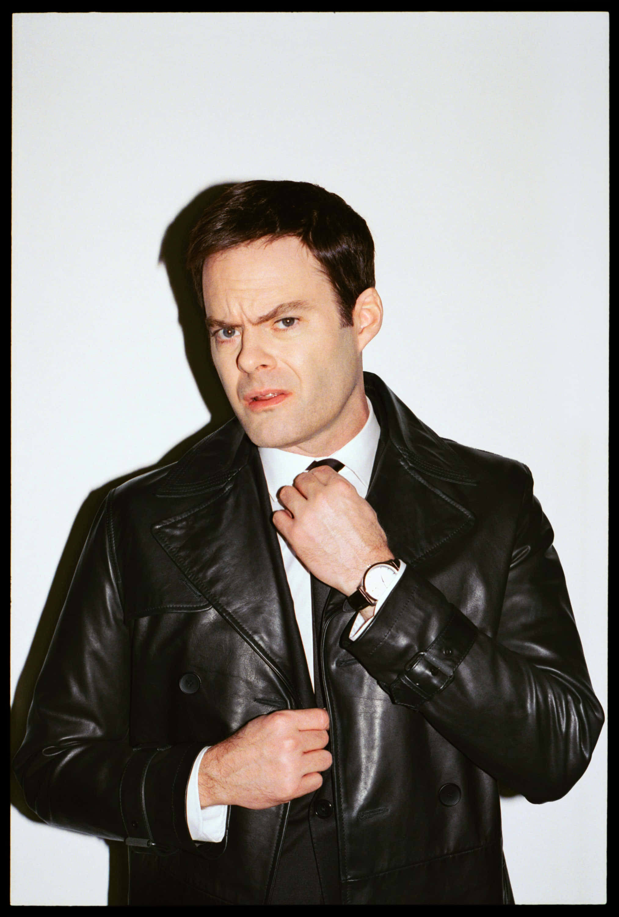 bill hader 桌布 壁紙 — 一名身穿黑色皮夾克的男子在純白背景及戲劇性陰影下整理領帶。