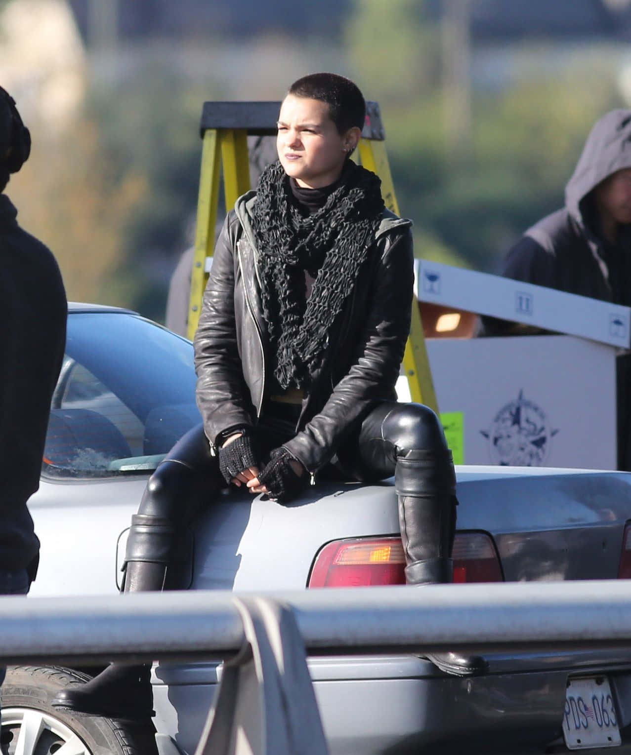 Negasonic Teenage Warhead 桌布 壁紙 — 一名身穿黑色皮革服裝的人坐在一輛銀色汽車上，電影佈景中可見工作人員和設備。