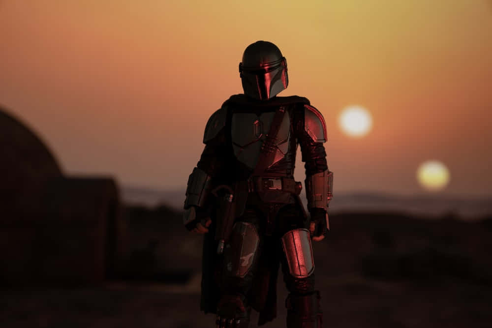 Star Wars Profile 桌布 壁紙 — 一名身穿黑色盔甲的曼達洛戰士在沙漠星球上以雙重日落為背景形成剪影。