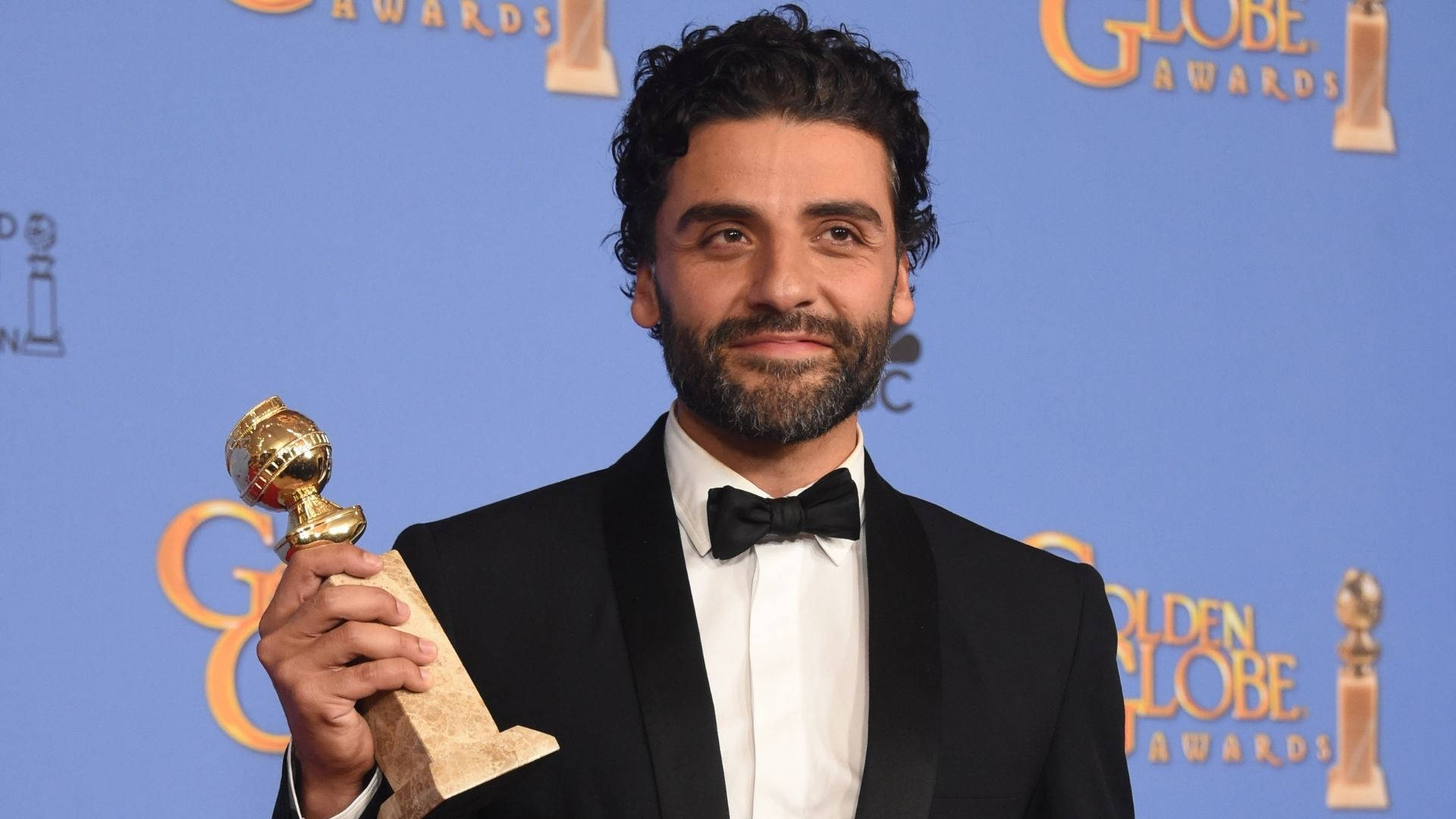 oscar 桌布 壁紙 — 一名身穿黑色禮服的男子在藍色背景前手持金球獎獎座，背景有活動標誌。