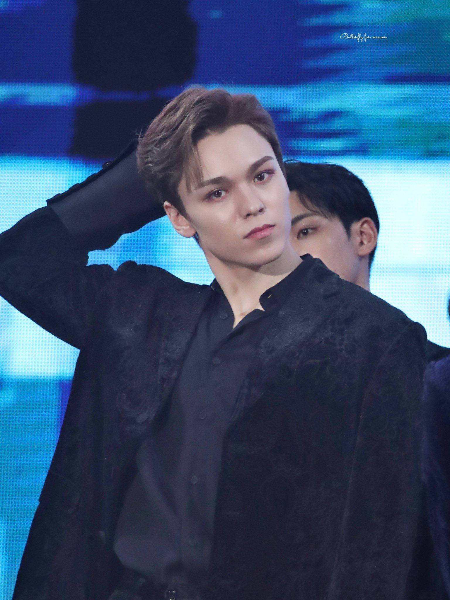 Vernon 桌布 壁紙 — 一名身穿黑色紋理外套的年輕男子在藍色燈光的舞台上自信地擺姿勢，身後有另一人部分可見。