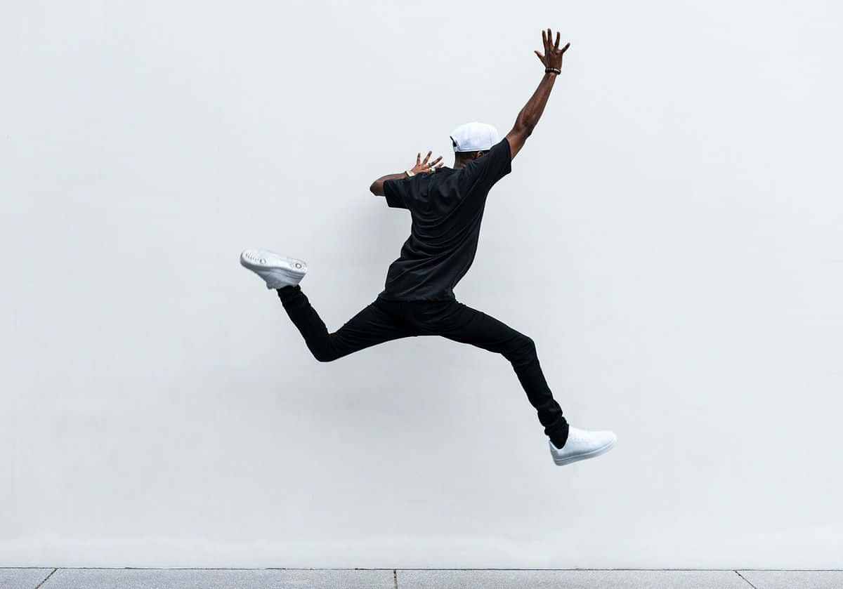 jump 桌布 壁紙 — 一名身穿黑色衣服、戴白色帽子的人，雙臂伸展，動態地跳向白色牆壁。