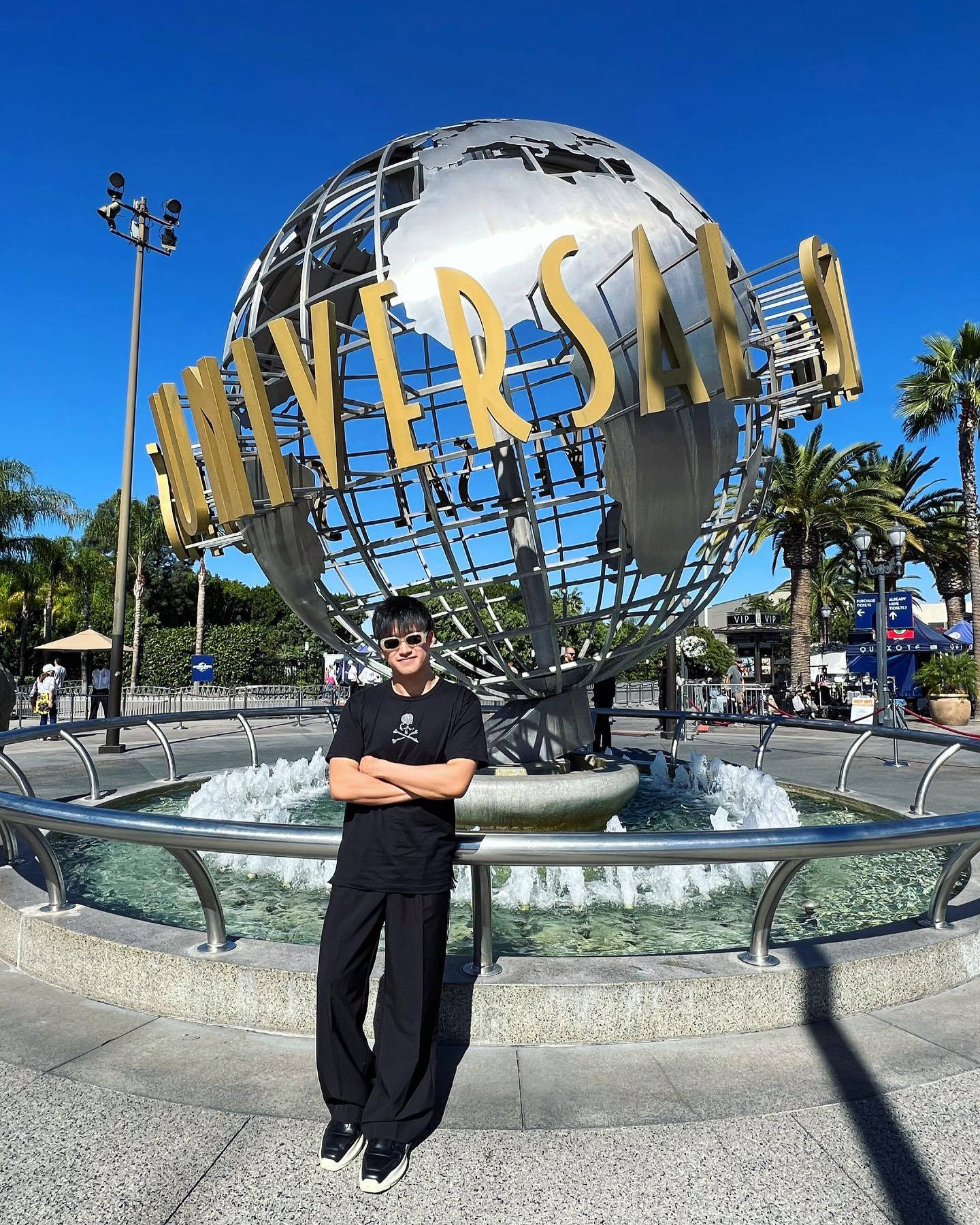 Universal Studios 桌布 壁紙 — 一名身穿黑色衣服的人自信地站在晴朗藍天下標誌性的環球影城地球噴泉前。