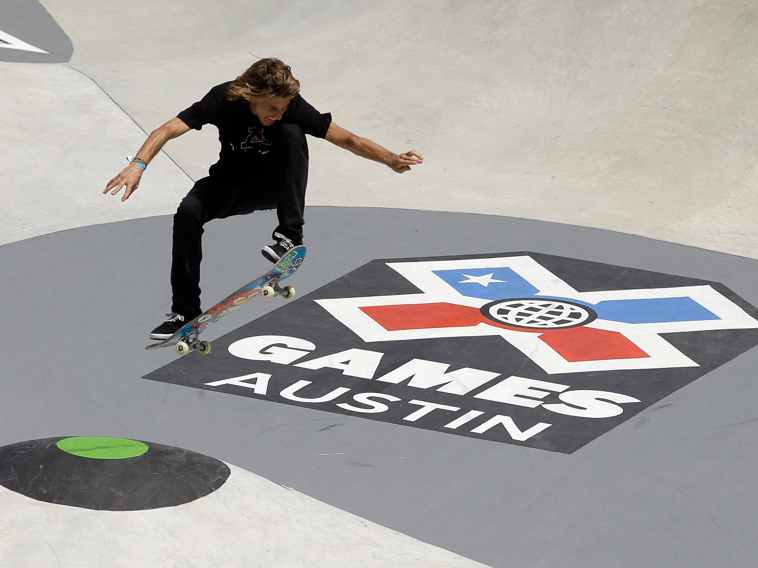 X 桌布 壁紙 — 一名身穿黑色衣服的滑板手在混凝土坡道上繪製的X Games Austin標誌上方表演技巧。