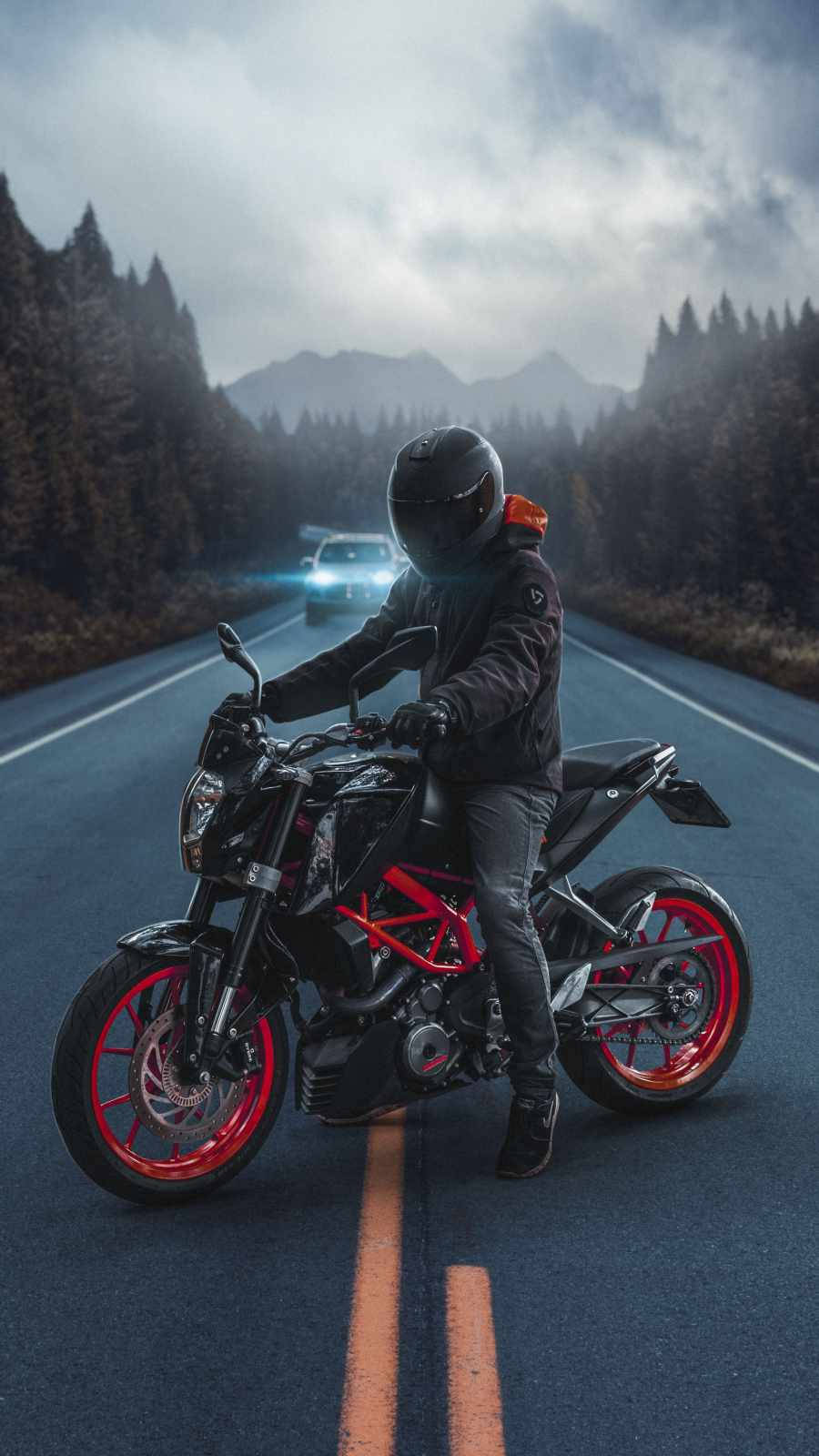 機車 桌布 壁紙 — 一名身穿黑色裝備的機車騎士在蜿蜒的道路上停下，紅色輪胎，一輛汽車在多雲的天空下駛近。