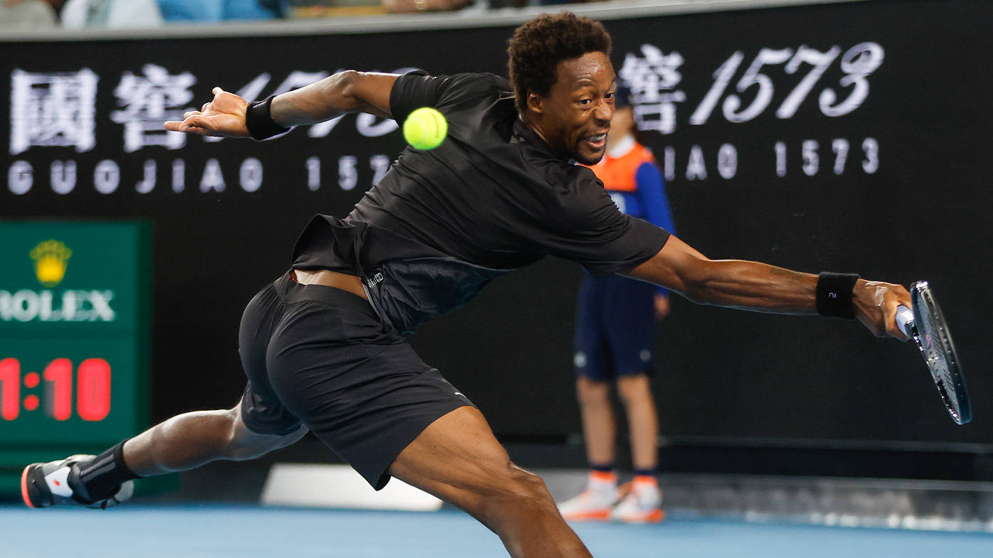 Athletic 桌布 壁紙 — 一名身穿黑色裝備的男網球選手在藍色球場上進行激烈比賽時，向前猛撲擊打一個亮黃色的球。