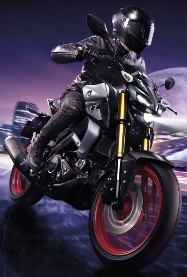 yamaha mt 15 桌布 壁紙 — 一名身穿黑色裝備的騎士在黃昏時分，在模糊的城市天際線背景下，騎著一輛帶有發光紅色輪圈的時尚運動摩托車傾斜入彎。