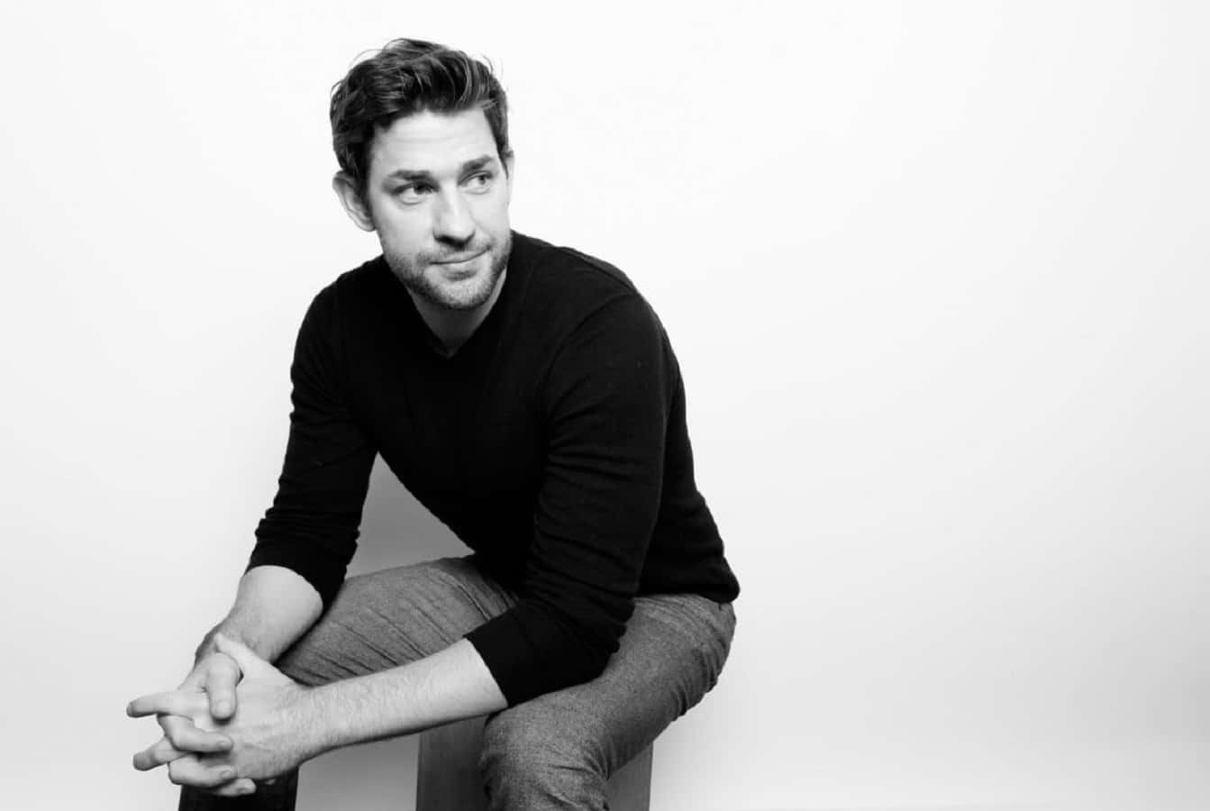 john krasinski 桌布 壁紙 — 一名身穿黑色襯衫的男子，在純白色背景前隨意地坐著，呈現黑白肖像。