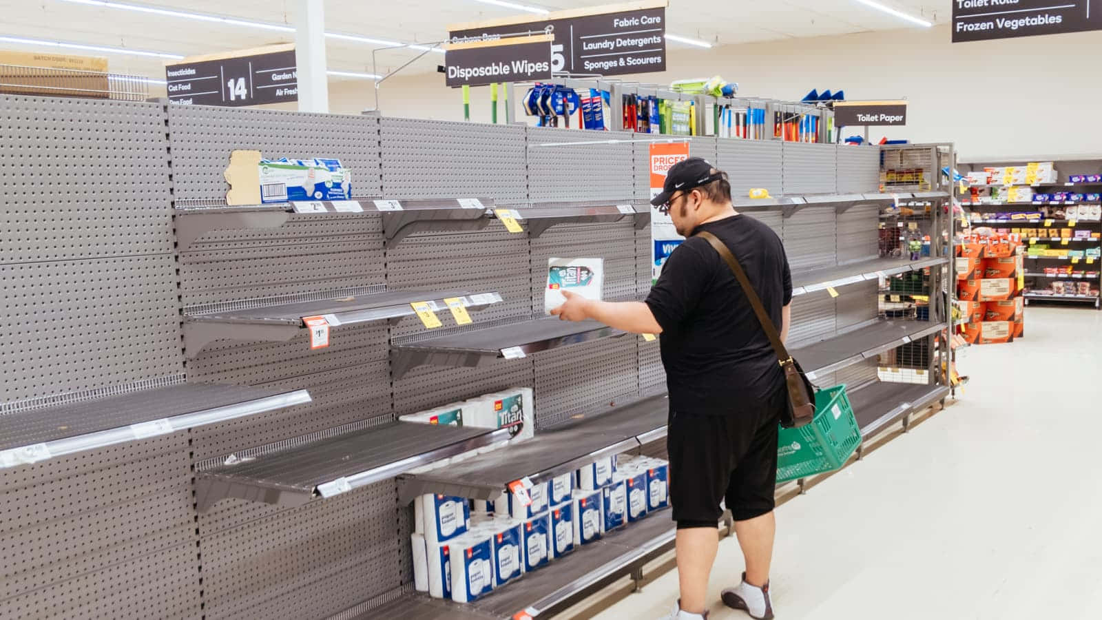Shopping 桌布 壁紙 — 一名身穿黑色襯衫的男子瀏覽著幾乎空無一物的超市貨架，架上只有幾盒濕紙巾和衛生紙。