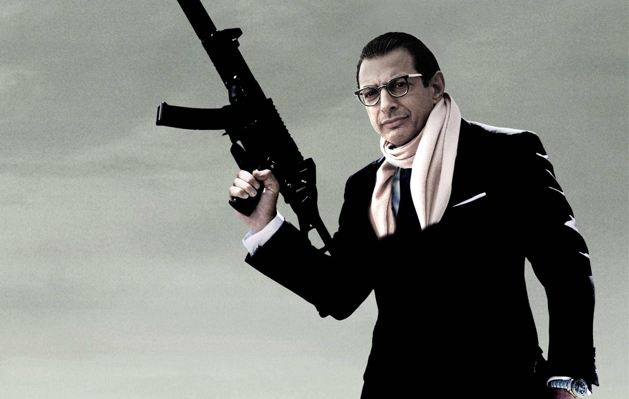 jeff goldblum 桌布 壁紙 — 一名身穿黑色西裝、戴眼鏡的男子，在柔和的灰色背景下手持突擊步槍。