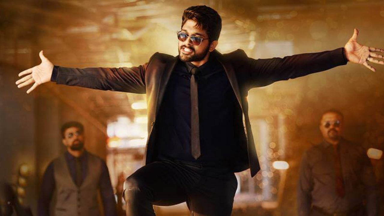 Allu Arjun 桌布 壁紙 — 一名身穿黑色西裝和太陽眼鏡的男子，在溫暖的金色散景背景下，張開雙臂歡快地跳躍。