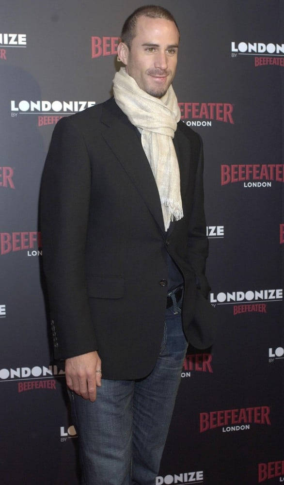 Actors 桌布 壁紙 — 一名身穿黑色西裝外套和奶油色圍巾的男子，在Beefeater London活動中自信地站在品牌背景前。