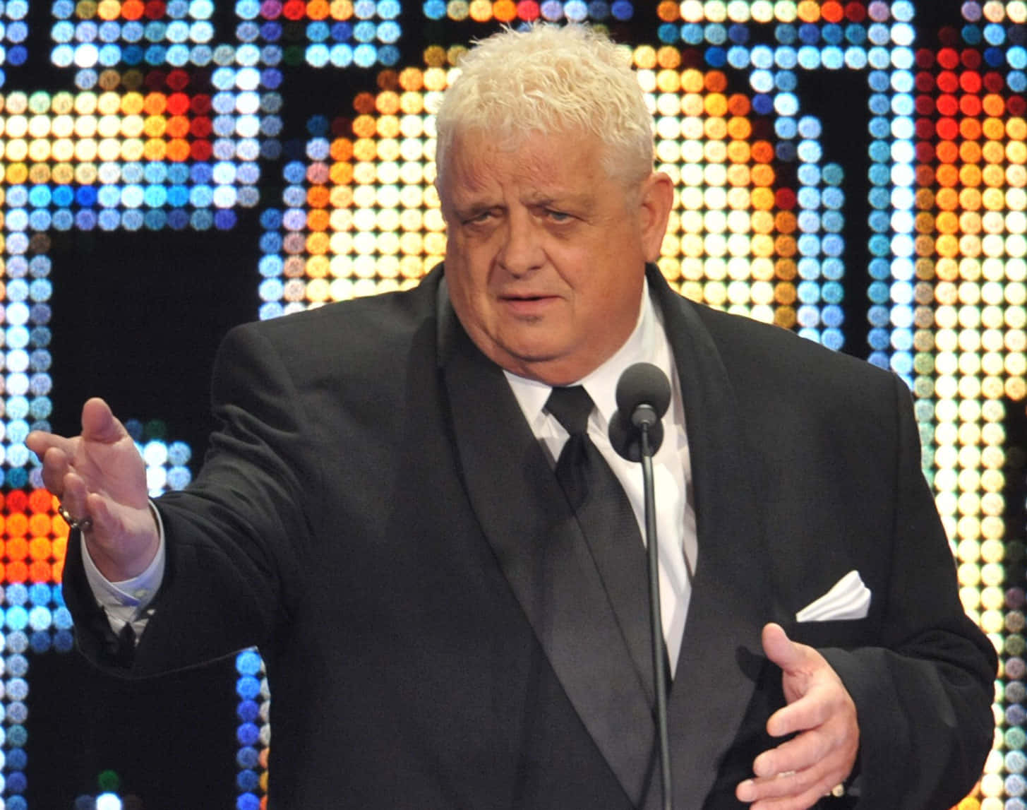 Dusty Rhodes 桌布 壁紙 — 一名身穿黑色西裝的男子在充滿活力的像素LED背景前熱情地做手勢。