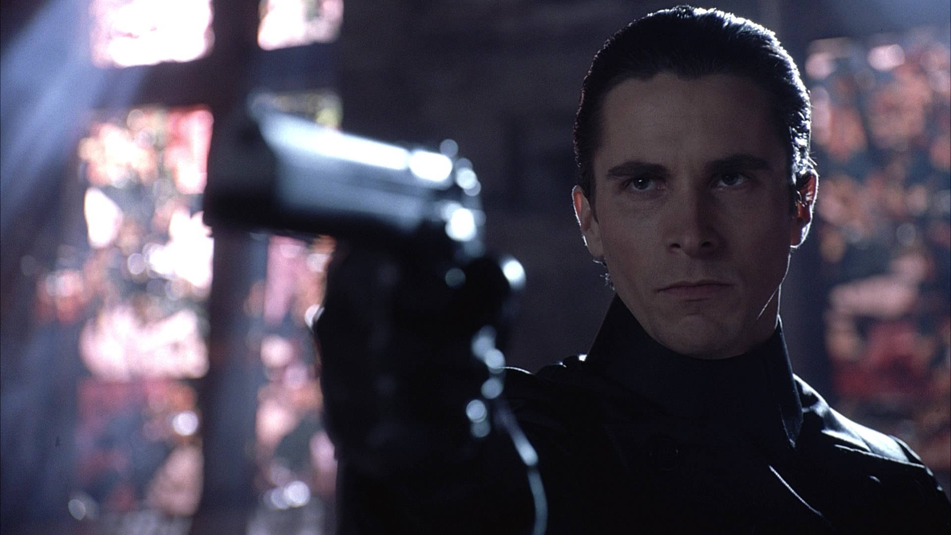 Christian Bale 桌布 壁紙 — 一名身穿黑色西裝的男子在模糊的彩色背景下專注地瞄準槍支。