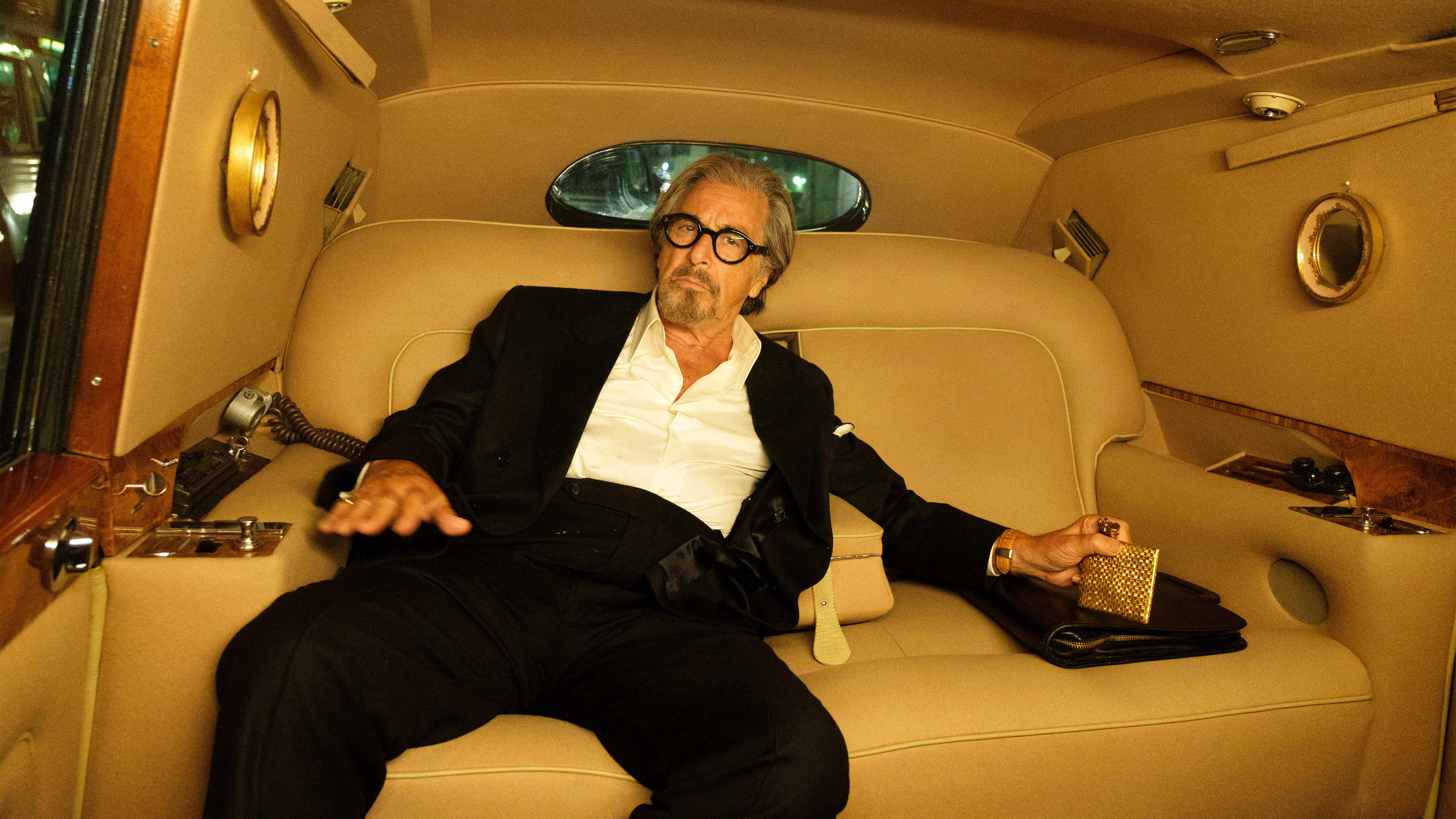 Al Pacino 桌布 壁紙 — 一名身穿黑色西裝的男子在豪華的奶油色皮革豪華轎車內放鬆，手持金色手拿包。