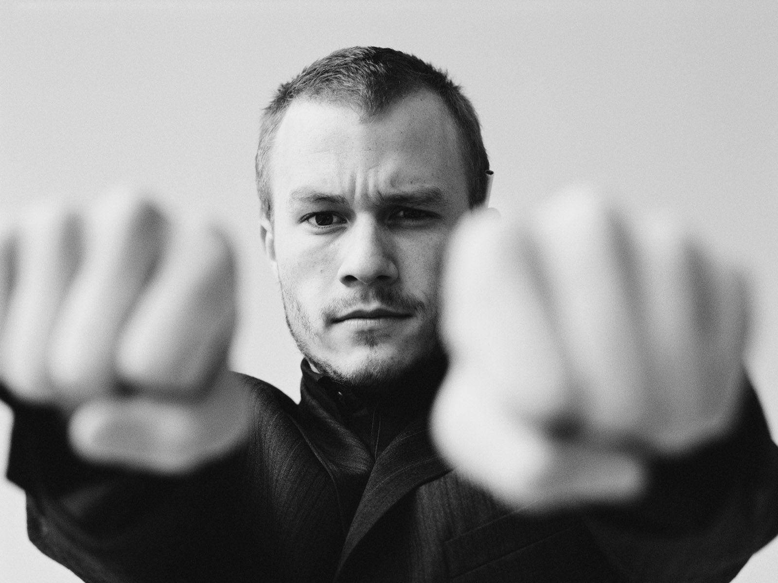 Heath Ledger 桌布 壁紙 — 一名身穿黑色西裝的男子緊握拳頭，前景模糊，目光銳利地凝視。