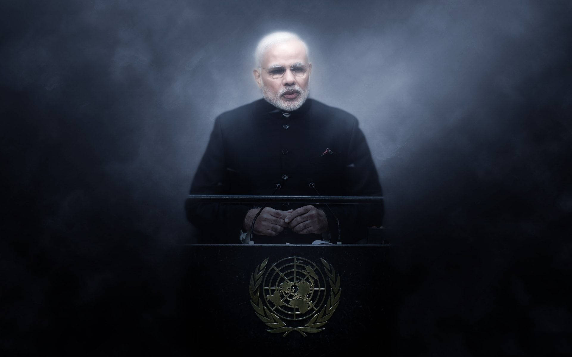 Narendra Modi 桌布 壁紙 — 一名身穿黑色西裝的男子莊嚴地站在帶有聯合國標誌的講台後面，戲劇性的聚光燈穿透黑暗的煙霧。